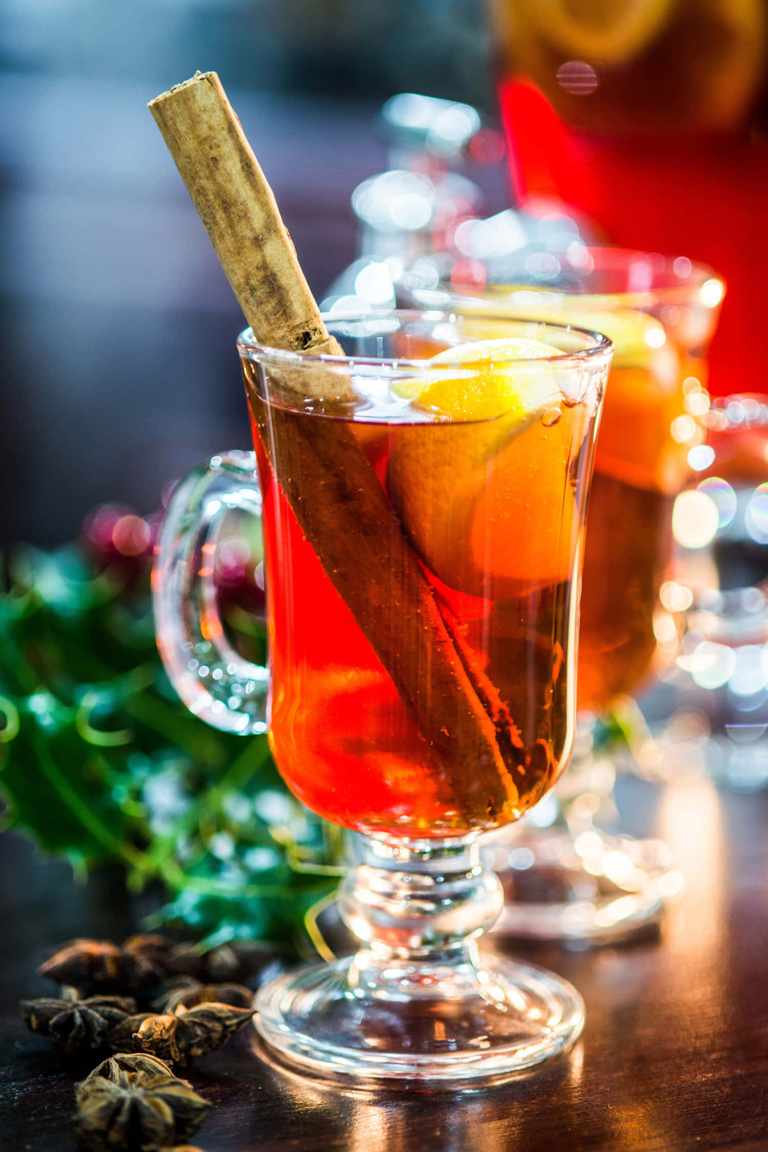 Winter Drinks 桌布 壁紙 — 一杯冒著熱氣的香料熱紅酒，搭配肉桂棒和柳橙片，在木桌上散發溫暖的光芒。