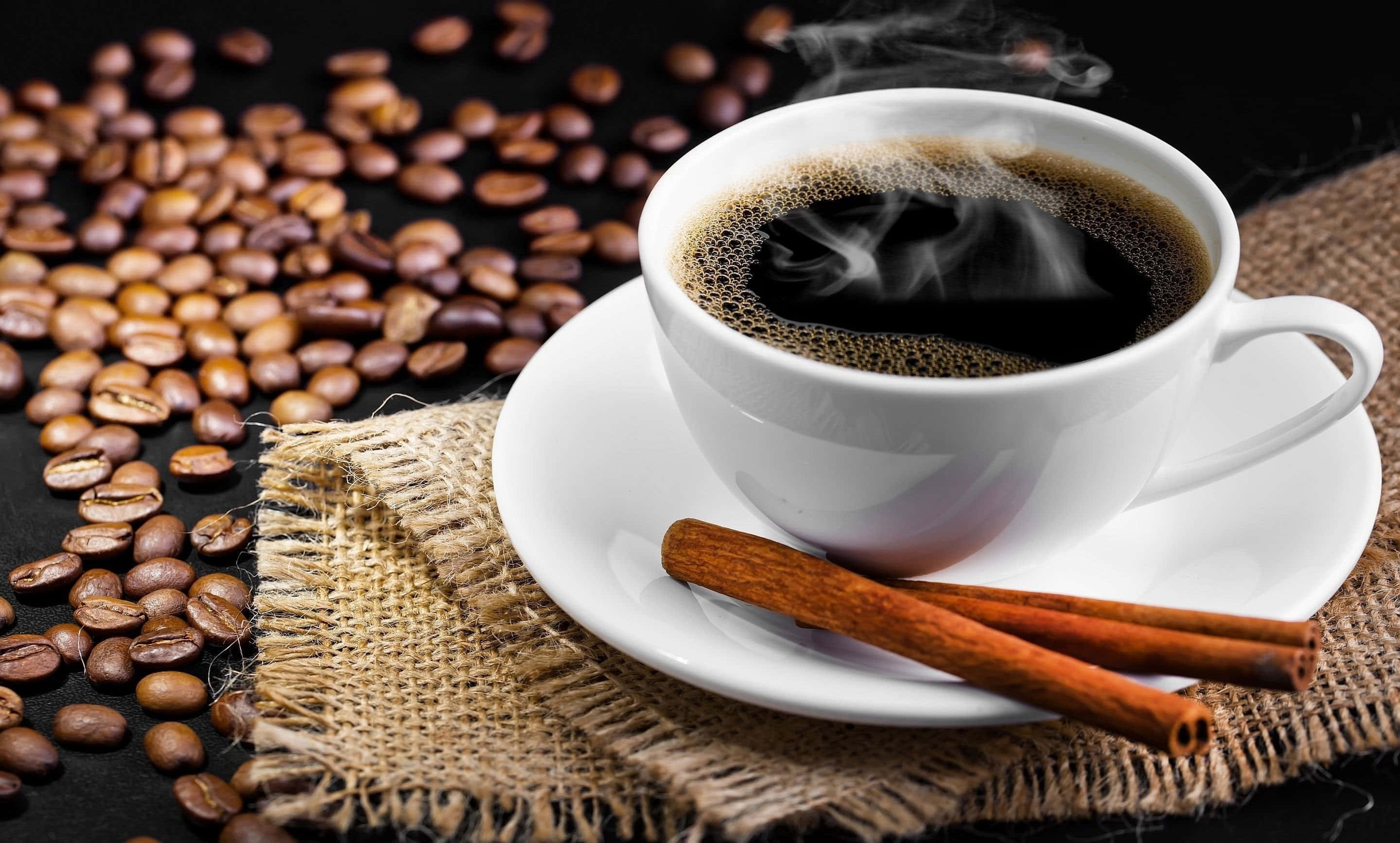 Black Coffee 桌布 壁紙 — 一杯冒著熱氣的黑咖啡搭配肉桂棒，放在麻布上的碟子裡，周圍散落著烘焙咖啡豆在深色表面上。