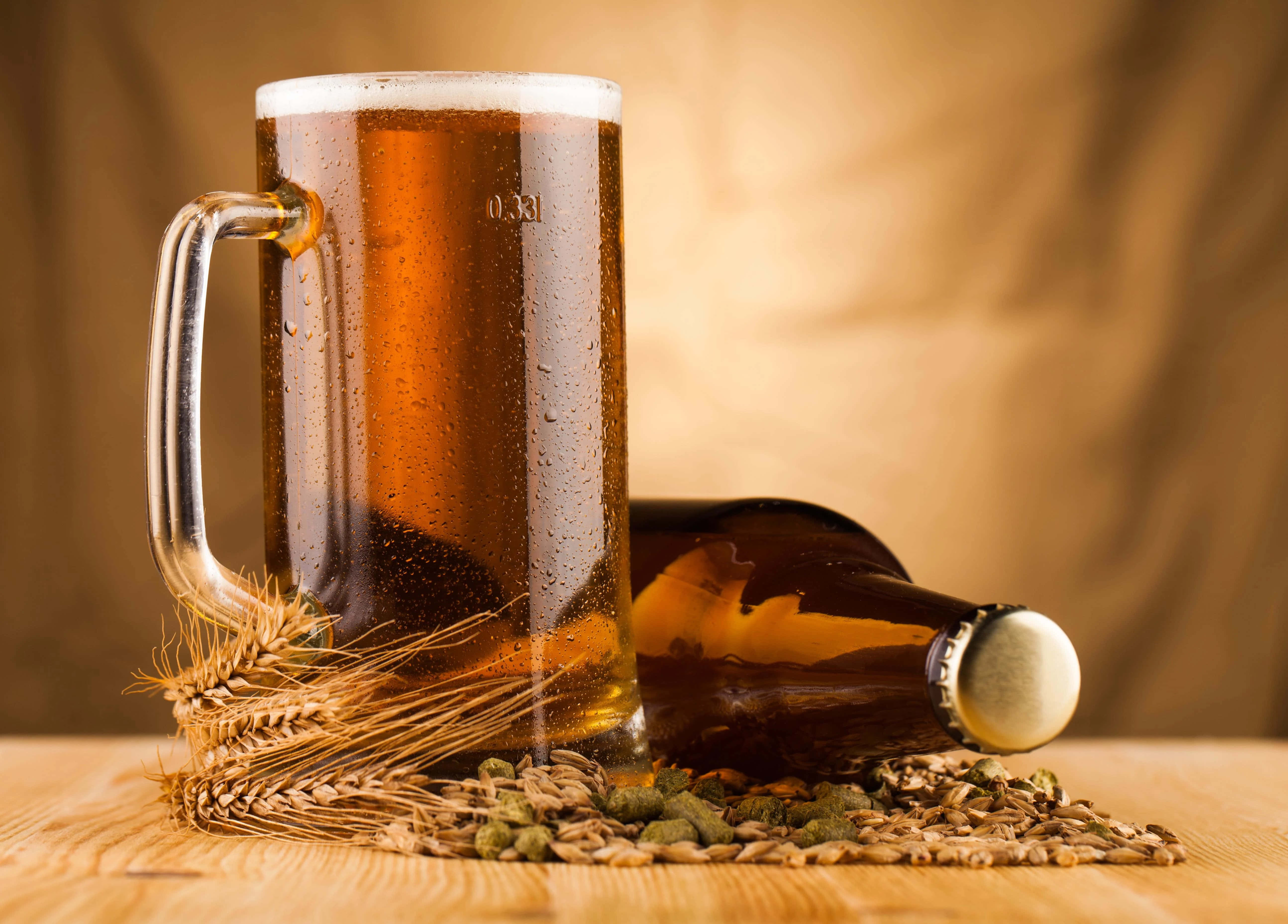 Beer 桌布 壁紙 — 一杯冰凍琥珀色啤酒，杯身凝結水珠，旁邊放著一瓶啤酒和小麥啤酒花，置於木桌上。