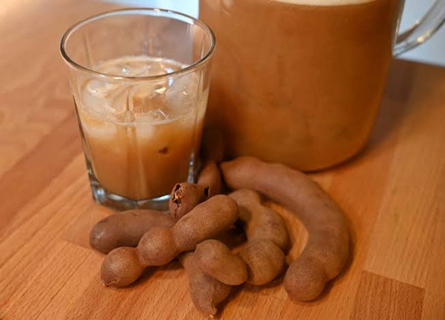 beans 桌布 壁紙 — 一杯冰凍羅望子飲料，連同整條羅望子莢，放在溫暖的木桌上。