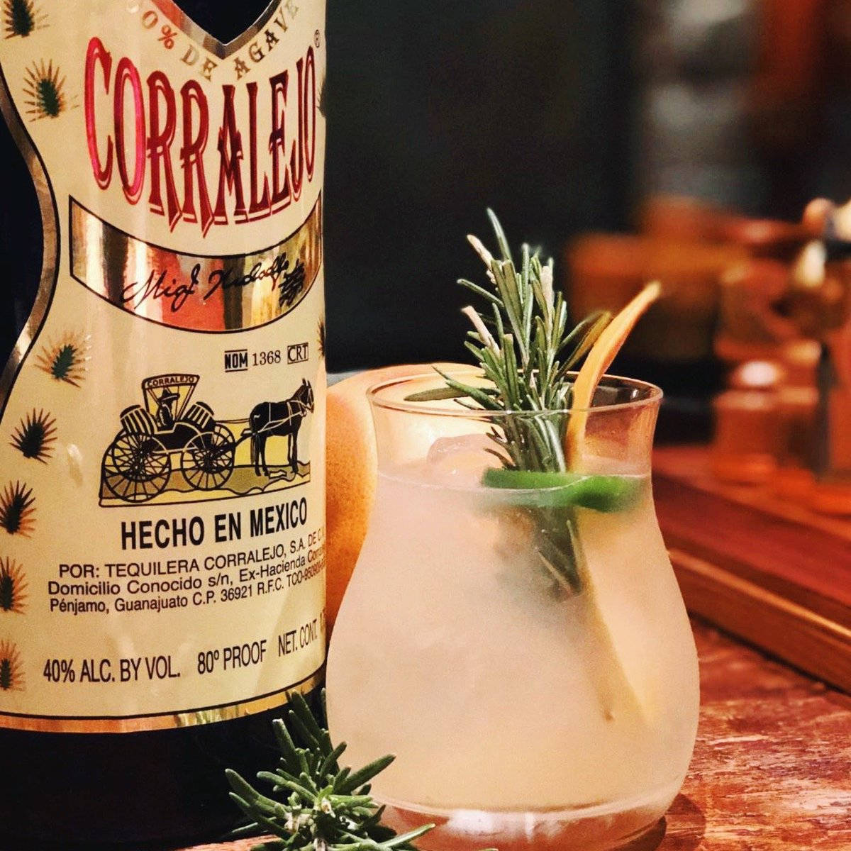 cocktail 桌布 壁紙 — 一杯冰涼的龍舌蘭雞尾酒，飾以迷迭香和柑橘，放在溫暖的木吧檯上，旁邊是一瓶 Corralejo。