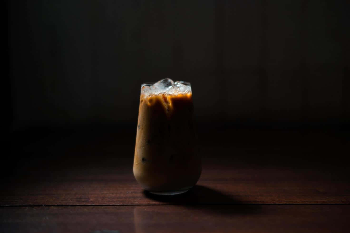 Milk And Coffee 桌布 壁紙 — 一杯加冰的冰咖啡放在深色木桌上，在戲劇性的低調燈光下。