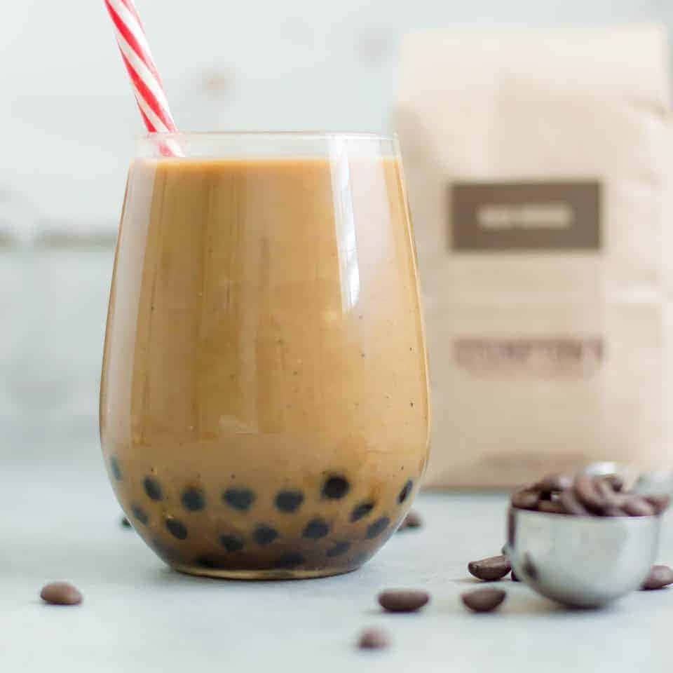 Boba Tea 桌布 壁紙 — 一杯奶油焦糖色的珍珠奶茶，內有黑色木薯珍珠，放在一個配有紅白條紋吸管的玻璃杯中。
