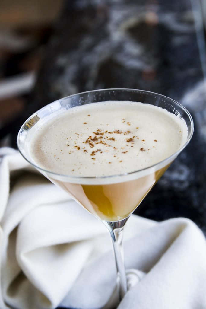 Winter Drinks 桌布 壁紙 — 一杯奶油雞尾酒盛載於馬丁尼杯中，以香料點綴，優雅地擺放在白色布料上，背景為深色大理石。