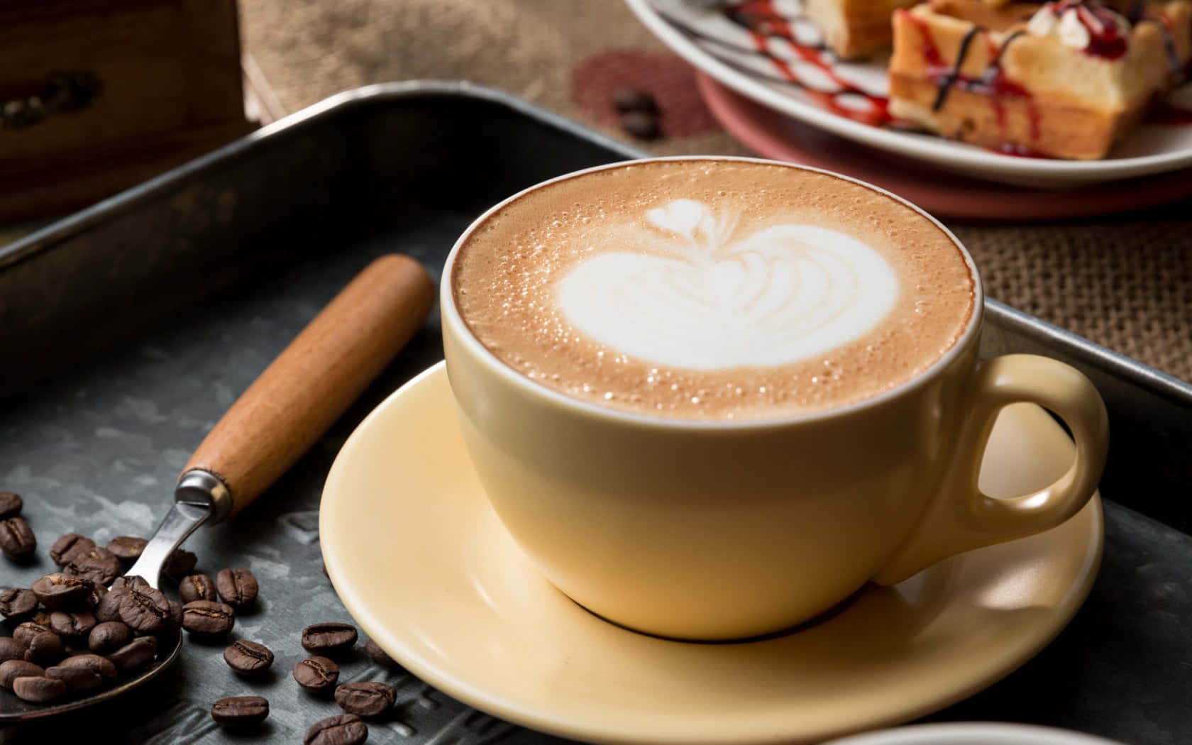 Milk And Coffee 桌布 壁紙 — 一杯奶白色咖啡拿鐵，上面有心形奶泡，放在米色杯子裡，旁邊有散落的咖啡豆和一盤鬆餅。