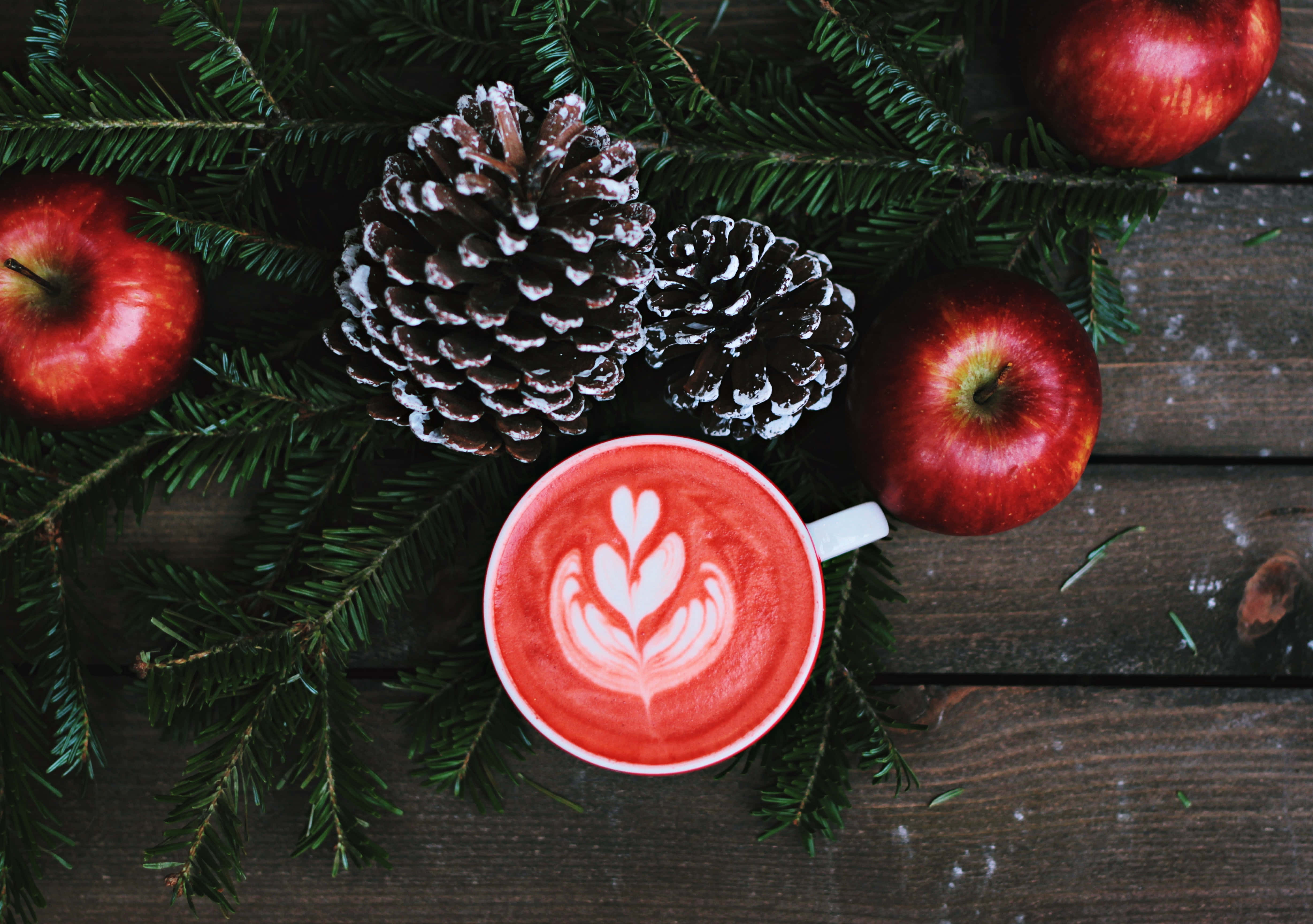 Latte Art 桌布 壁紙 — 一杯帶有心形拉花藝術的紅色拿鐵，放在鋪滿松果和紅蘋果的鄉村風格木桌上。