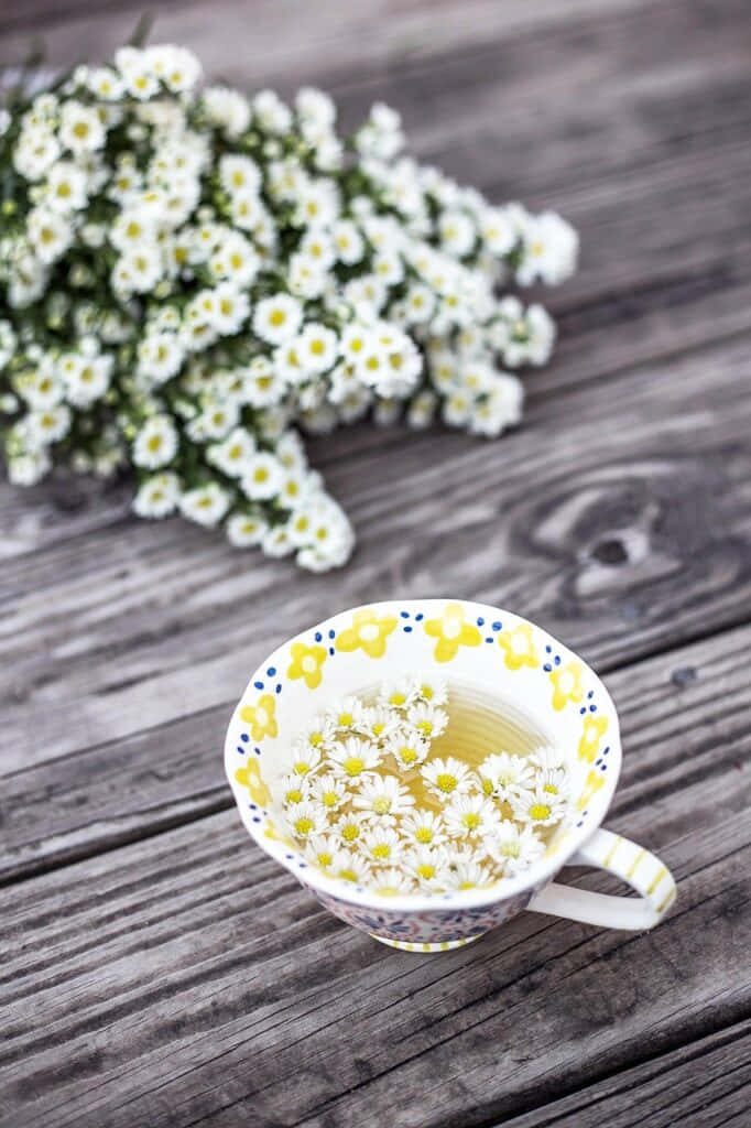 Morning Tea 桌布 壁紙 — 一杯帶有浮花的洋甘菊茶，旁邊放著一束花，在一張風化的木桌上。