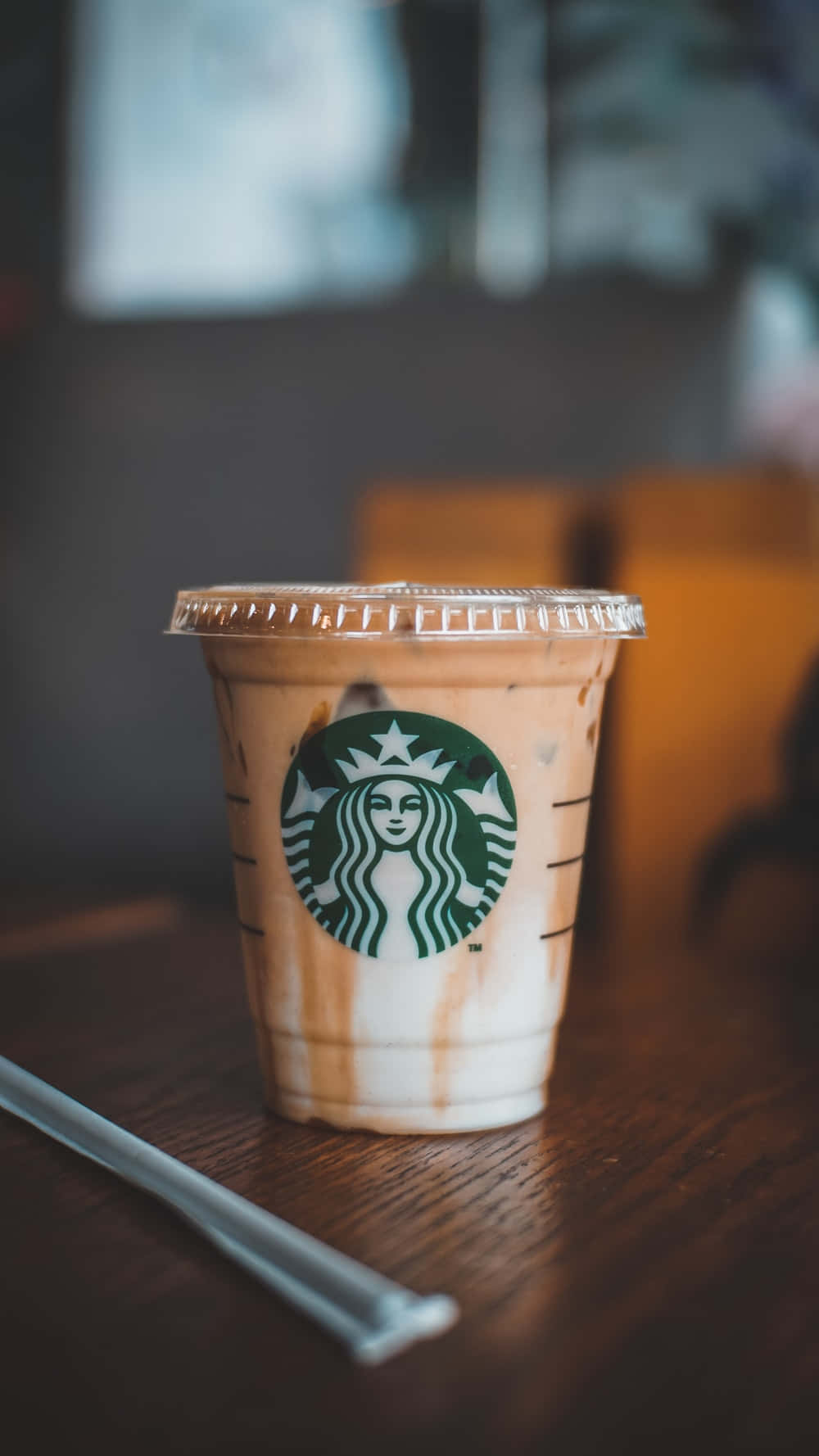 Aesthetic Starbucks 桌布 壁紙 — 一杯帶有焦糖醬的星巴克冰咖啡放在木桌上，旁邊有一根透明吸管。