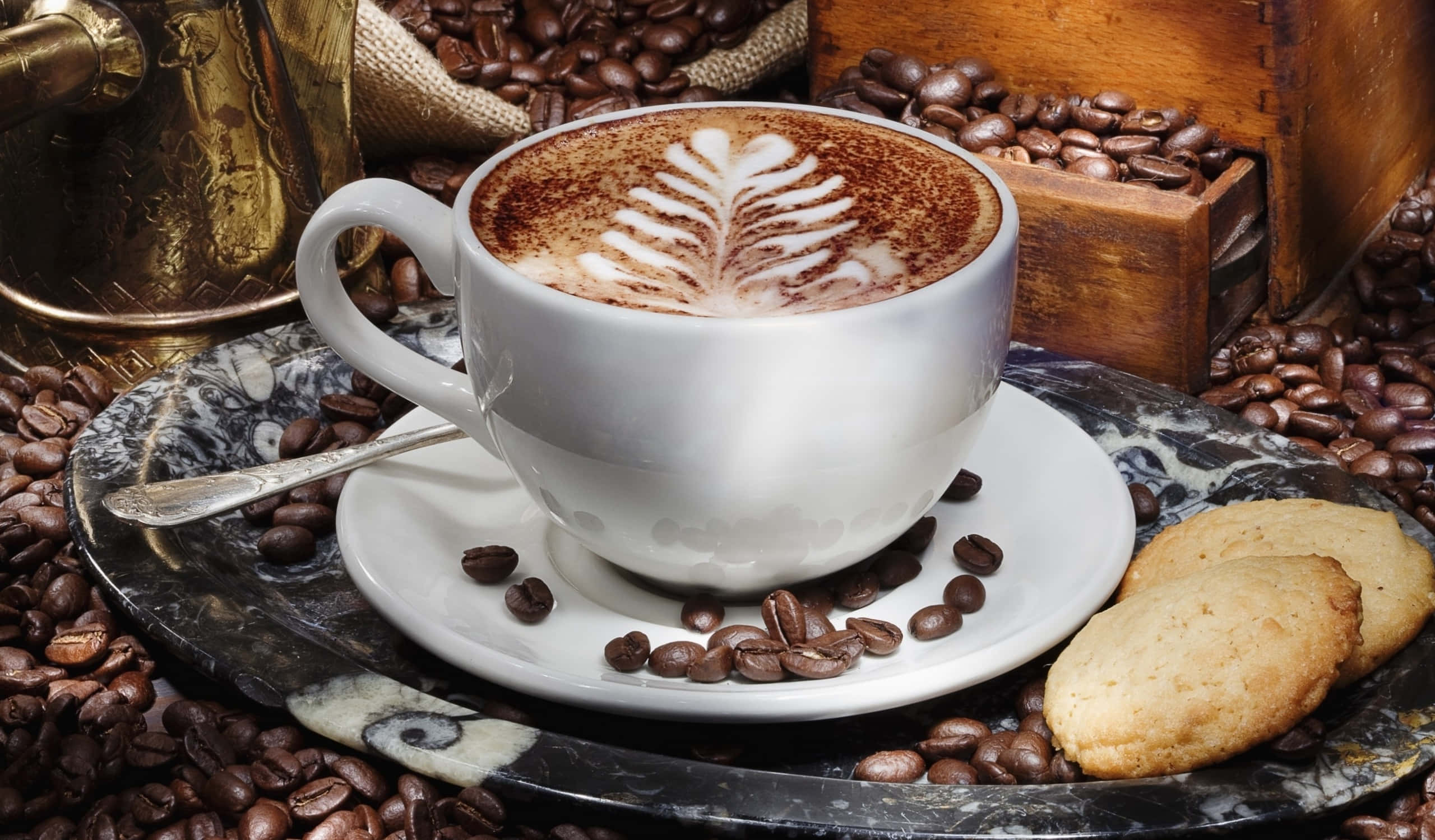 Morning Coffee 桌布 壁紙 — 一杯帶有葉子拉花藝術的白咖啡，放在一個被咖啡豆和餅乾包圍的大理石托盤上。