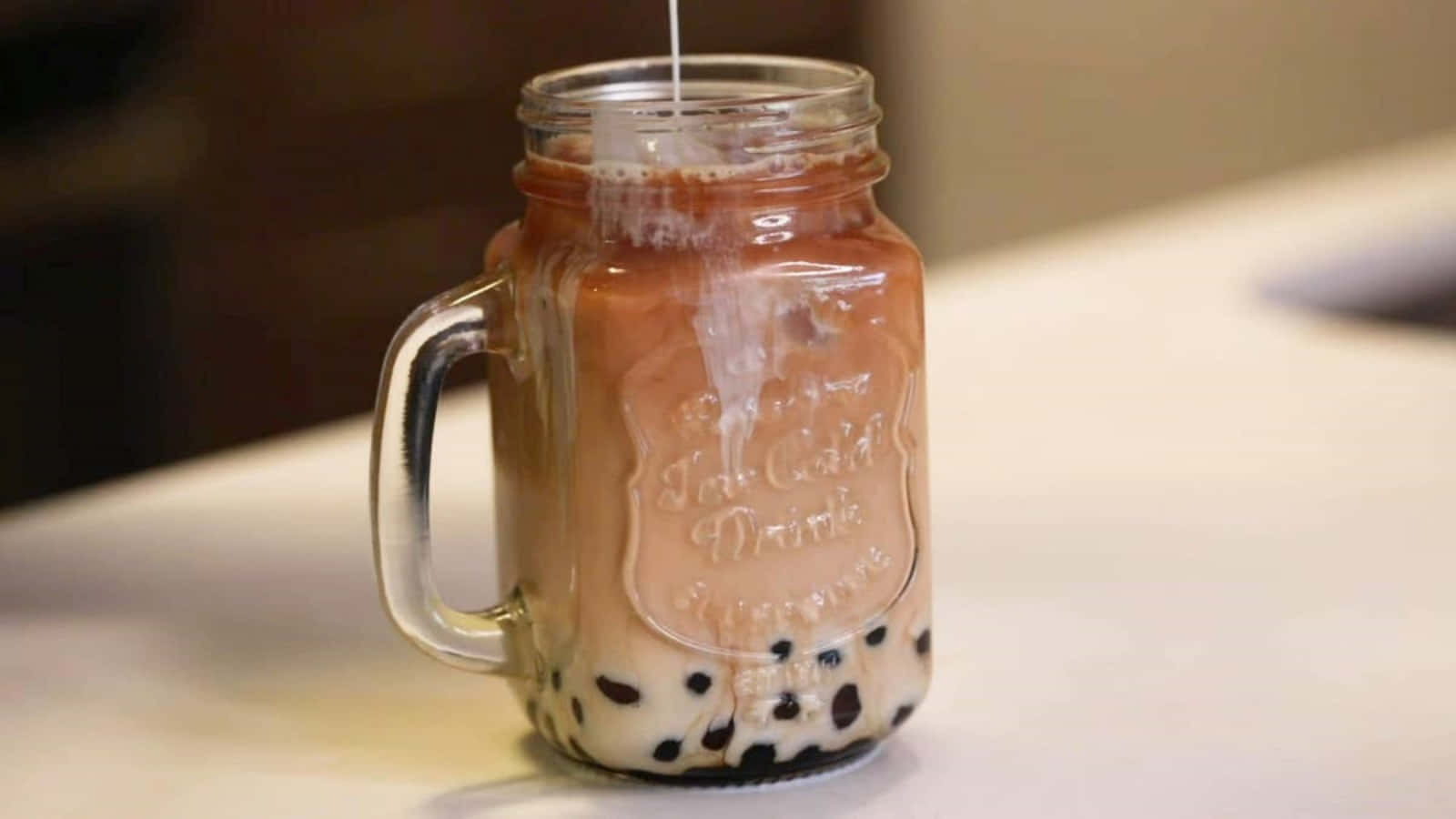 Boba Tea 桌布 壁紙 — 一杯帶有黑珍珠的奶油泡泡茶正在倒入白色檯面上的玻璃梅森罐中。