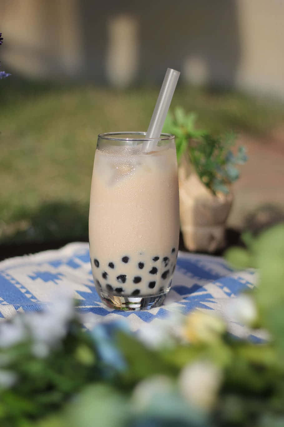 Boba Tea 桌布 壁紙 — 一杯帶有黑色珍珠的奶油泡泡茶，放在戶外藍色圖案布上的高腳杯中。