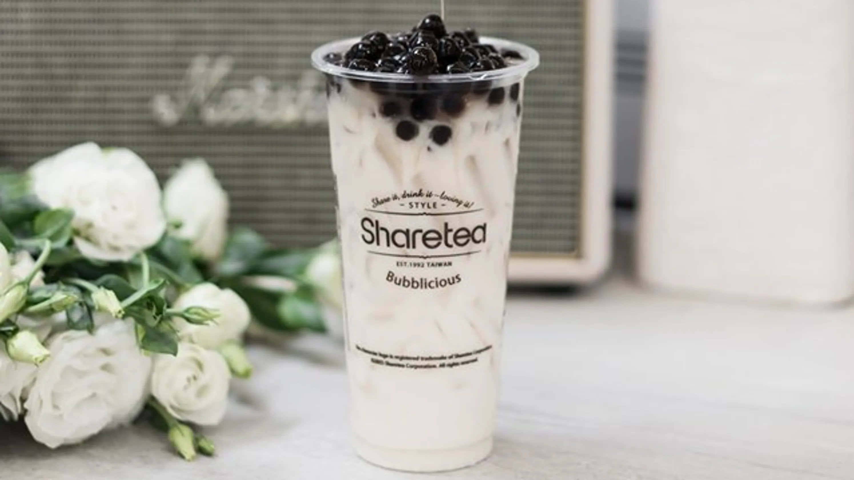 Boba Tea 桌布 壁紙 — 一杯帶有黑色珍珠的奶油狀Sharetea泡泡奶茶，放在木桌上，旁邊是白玫瑰。