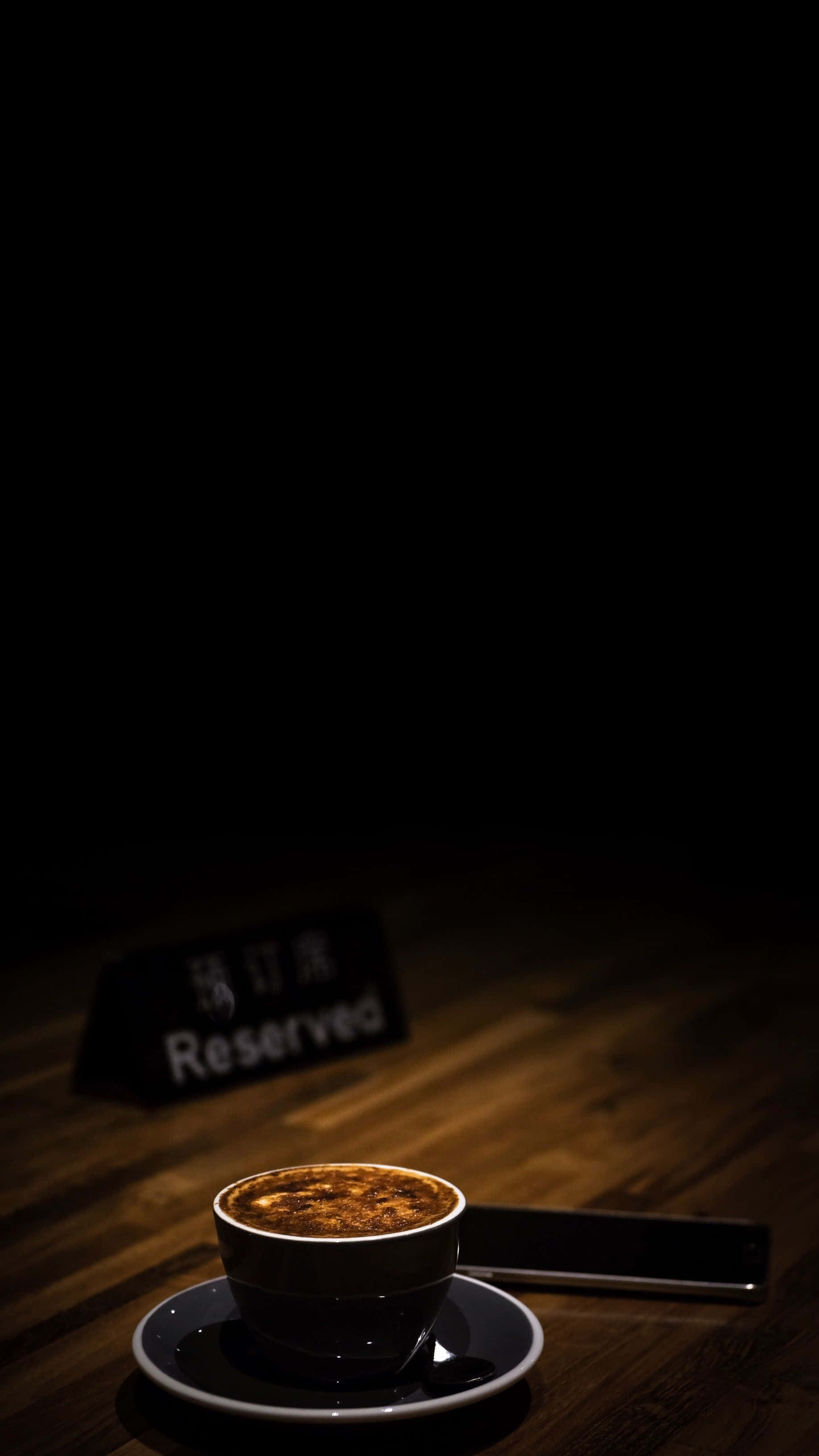 Reserved 桌布 壁紙 — 一杯暖光照耀的濃縮咖啡放在木桌上，旁邊有電話和已預訂的牌子，身處燈光昏暗的咖啡館。