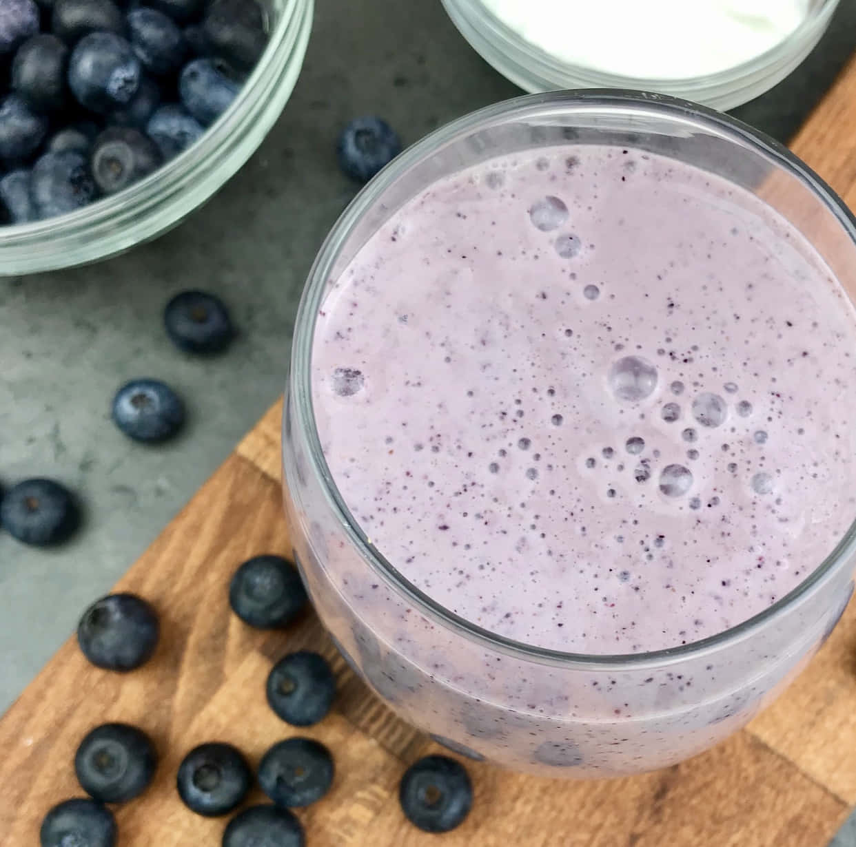 Blueberry Smoothie 桌布 壁紙 — 一杯泡沫紫色藍莓奶昔放在木板上，周圍是新鮮藍莓和優格。