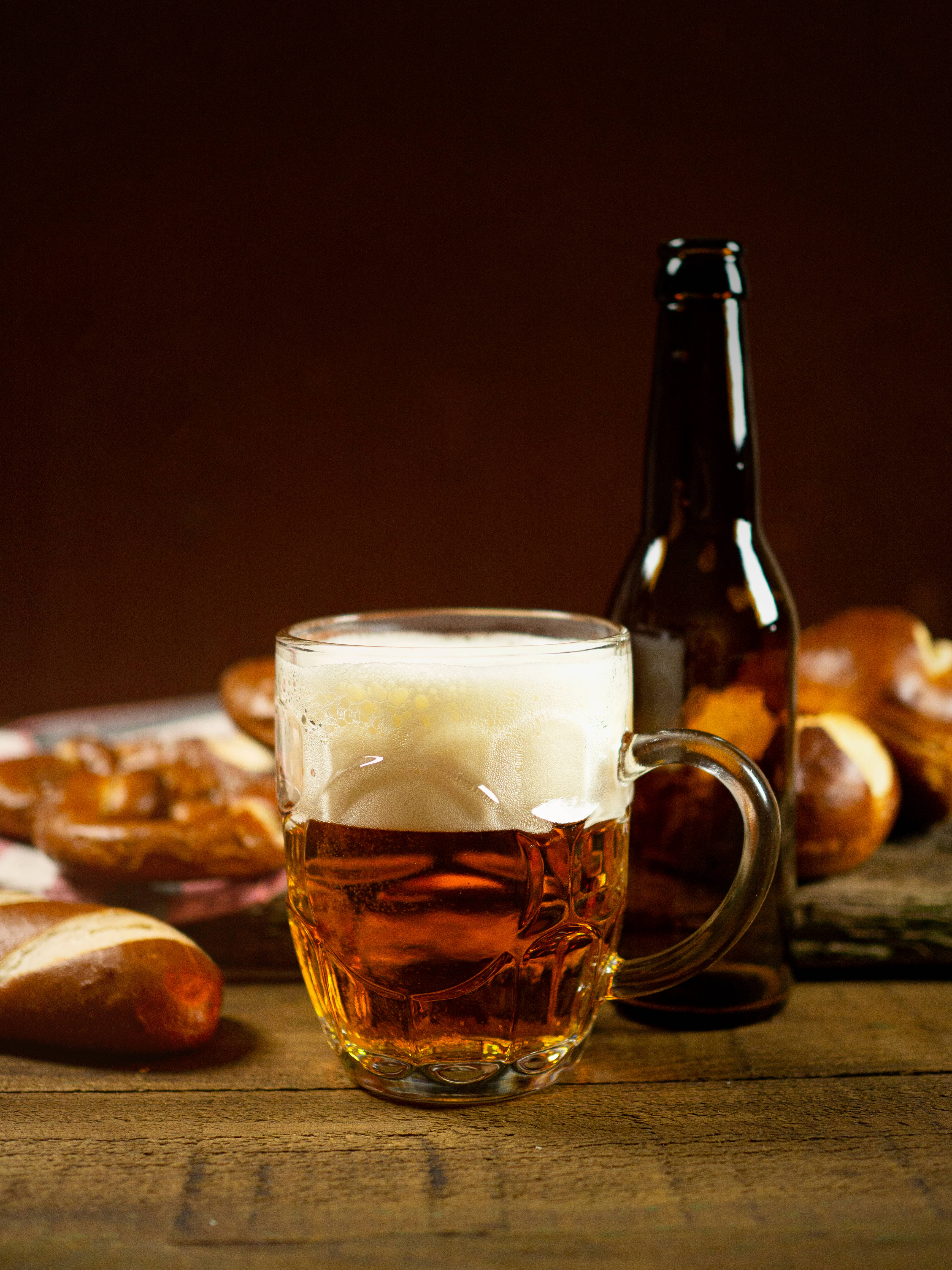 Beer 桌布 壁紙 — 一杯泡沫豐富的琥珀色啤酒放在玻璃杯中，旁邊有蝴蝶餅和瓶子，置於鄉村風格的木桌上。