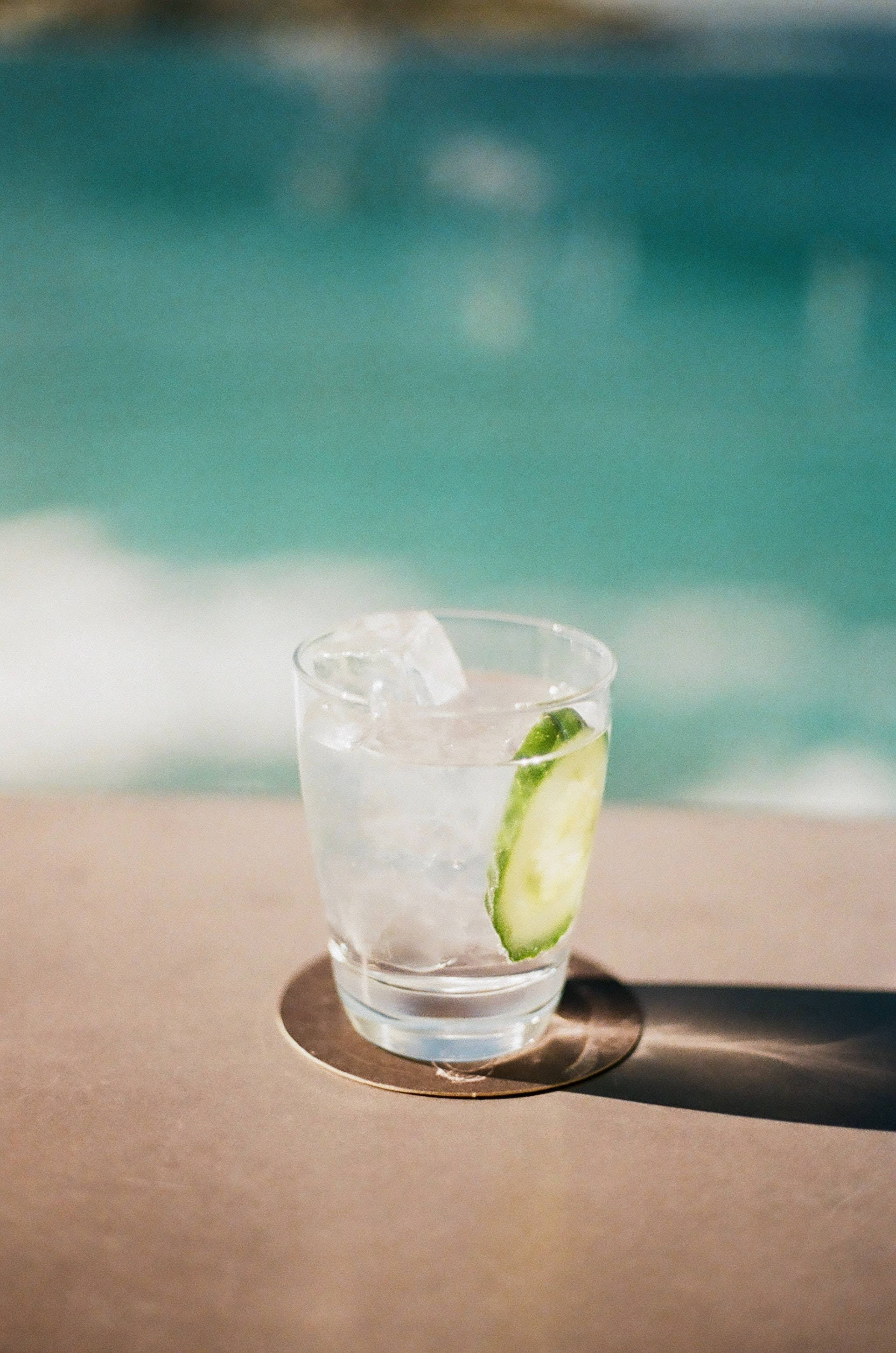 drinks 桌布 壁紙 — 一杯清爽的小黃瓜雞尾酒加冰，放在杯墊上，旁邊是碧藍的泳池，在明亮的陽光下。