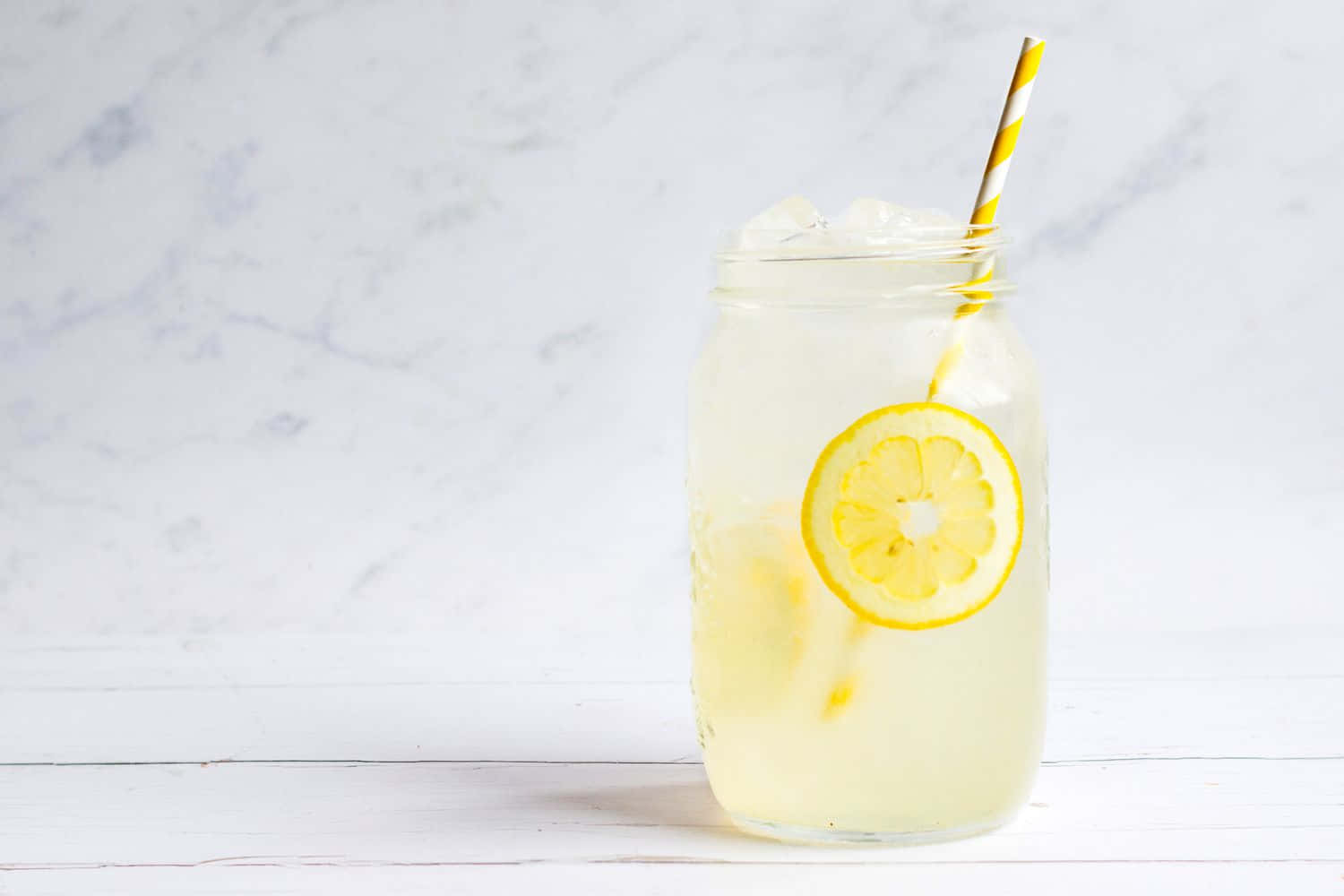 Lemonade 桌布 壁紙 — 一杯清爽的檸檬水，裝在梅森罐裡，加冰和條紋吸管，放在白色木質表面上，背景是大理石。