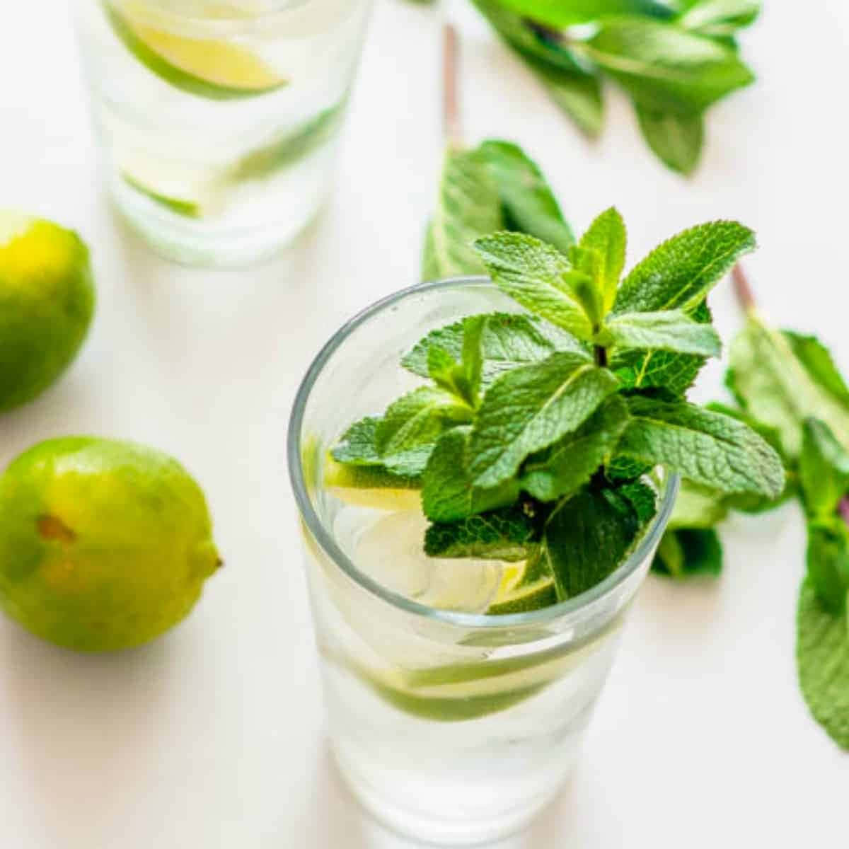 Lime 桌布 壁紙 — 一杯清爽的薄荷萊姆水放在明亮的白色表面上，旁邊有整個萊姆和散落的薄荷葉。