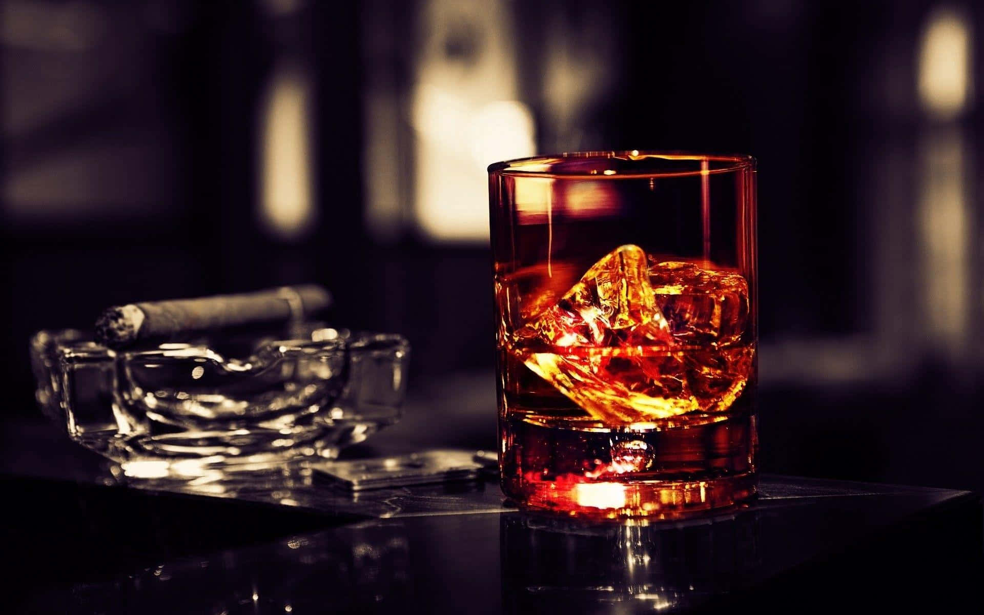 alcohol 桌布 壁紙 — 一杯溫暖燈光照射下、加冰的威士忌放在昏暗酒廊的深色吧檯上，旁邊有一支雪茄。