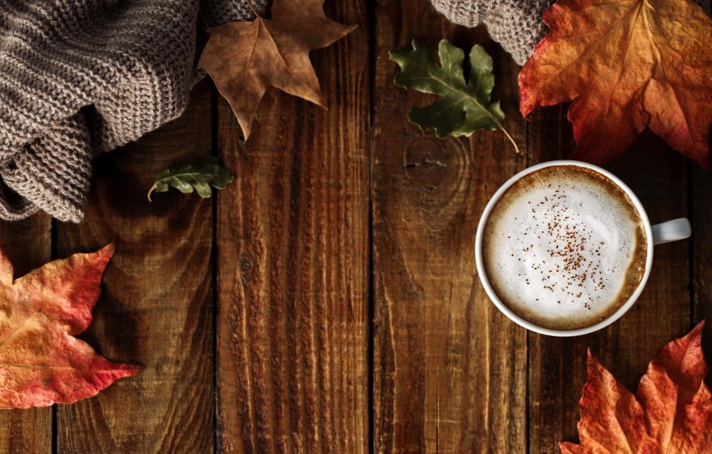 Coffee Aesthetic 桌布 壁紙 — 一杯溫暖的泡沫咖啡搭配肉桂，放在質樸的木桌上，周圍環繞著鮮豔的秋葉和一條針織圍巾。