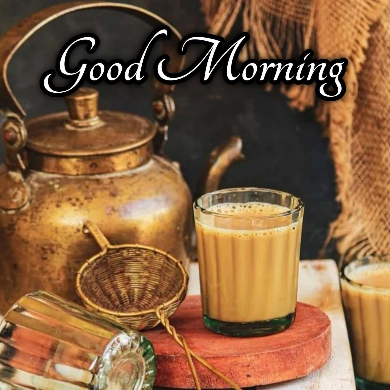 Morning Tea 桌布 壁紙 — 一杯溫暖的金色印度奶茶放在一個質樸的木板上，旁邊有一個復古黃銅水壺和編織過濾器。