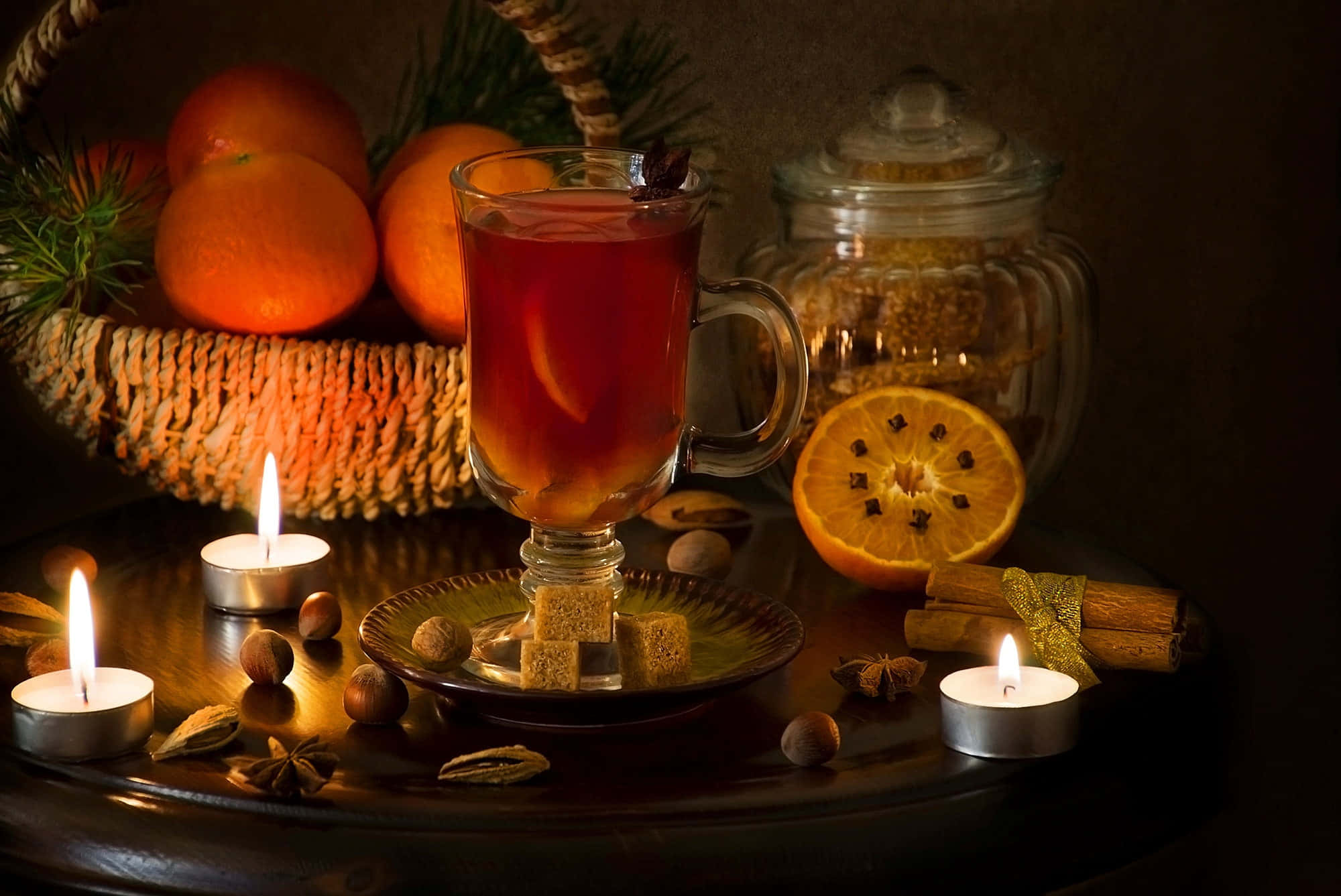 Mulled Wine 桌布 壁紙 — 一杯溫暖的香料茶在柳橙、肉桂和點燃的蠟燭旁閃耀，構成舒適的冬季靜物畫。