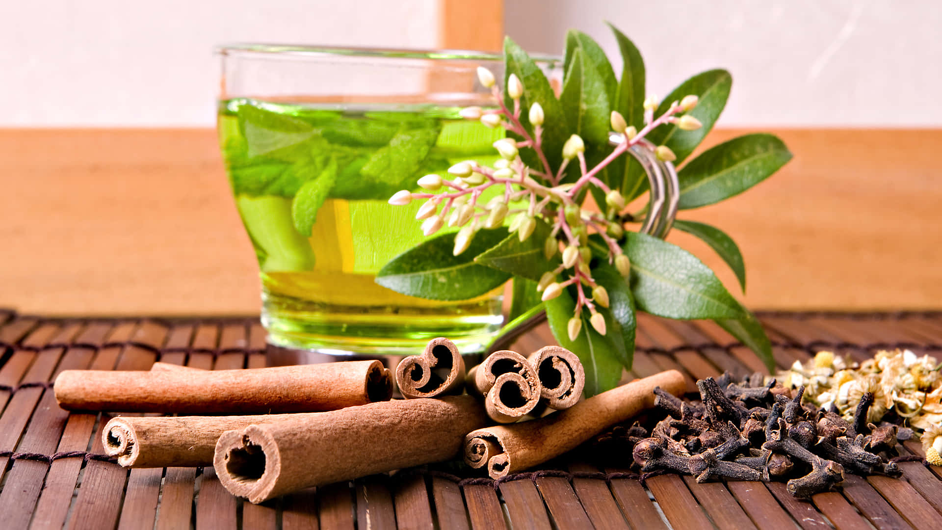 Floral Tea 桌布 壁紙 — 一杯漂浮著薄荷葉的綠色花草茶，旁邊放著肉桂棒、丁香和新鮮綠色植物，在竹蓆上。