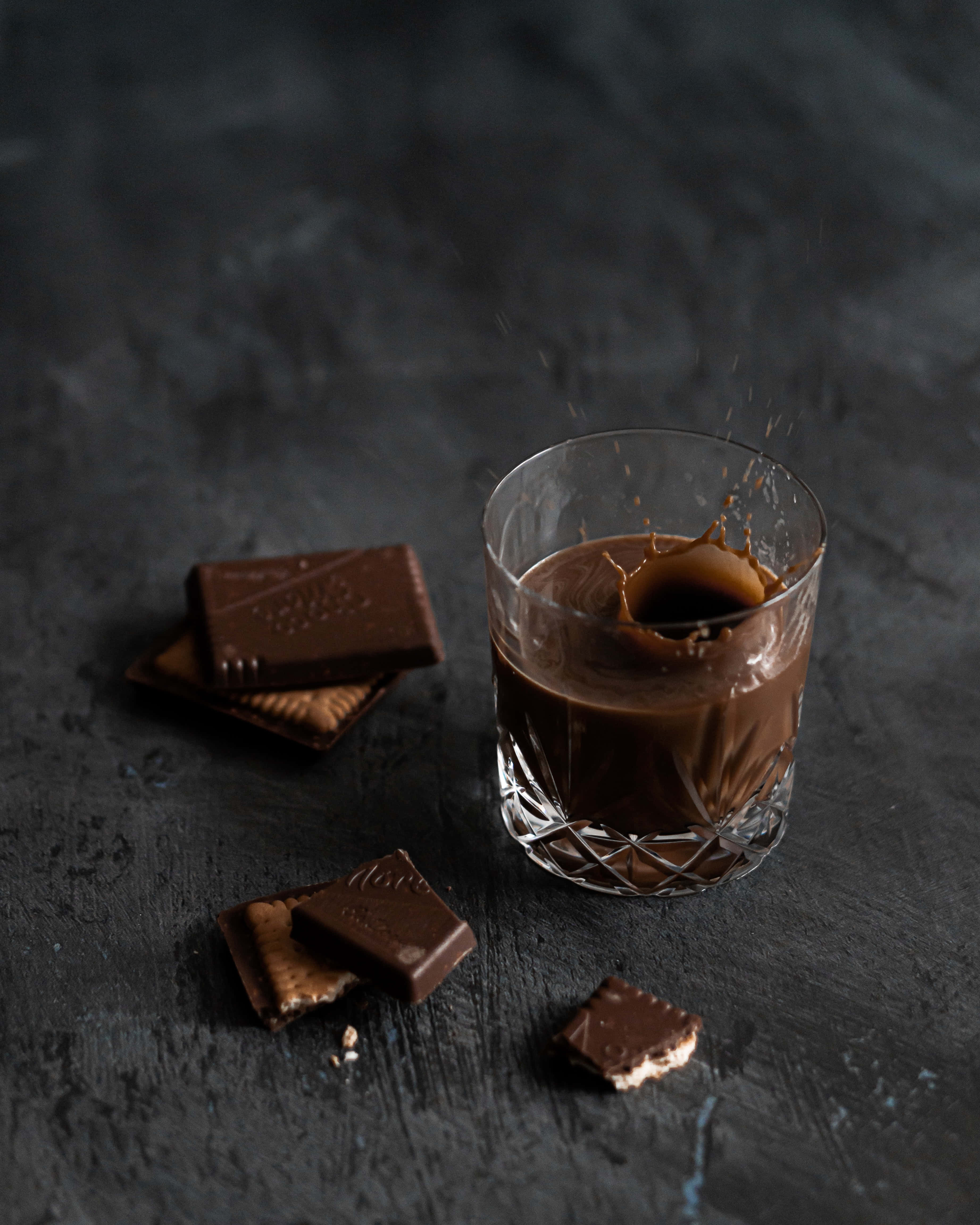 Dark Chocolate 桌布 壁紙 — 一杯濃郁的融化巧克力飛濺，巧克力碎片散落在深色紋理表面上。