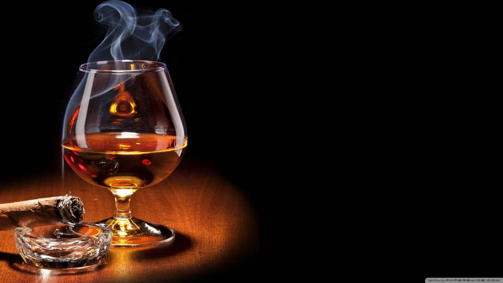 Drink 桌布 壁紙 — 一杯煙霧繚繞的琥珀色威士忌在黑色背景的木桌上，旁邊的水晶煙灰缸裡放著一支點燃的雪茄，散發著溫暖的光芒。