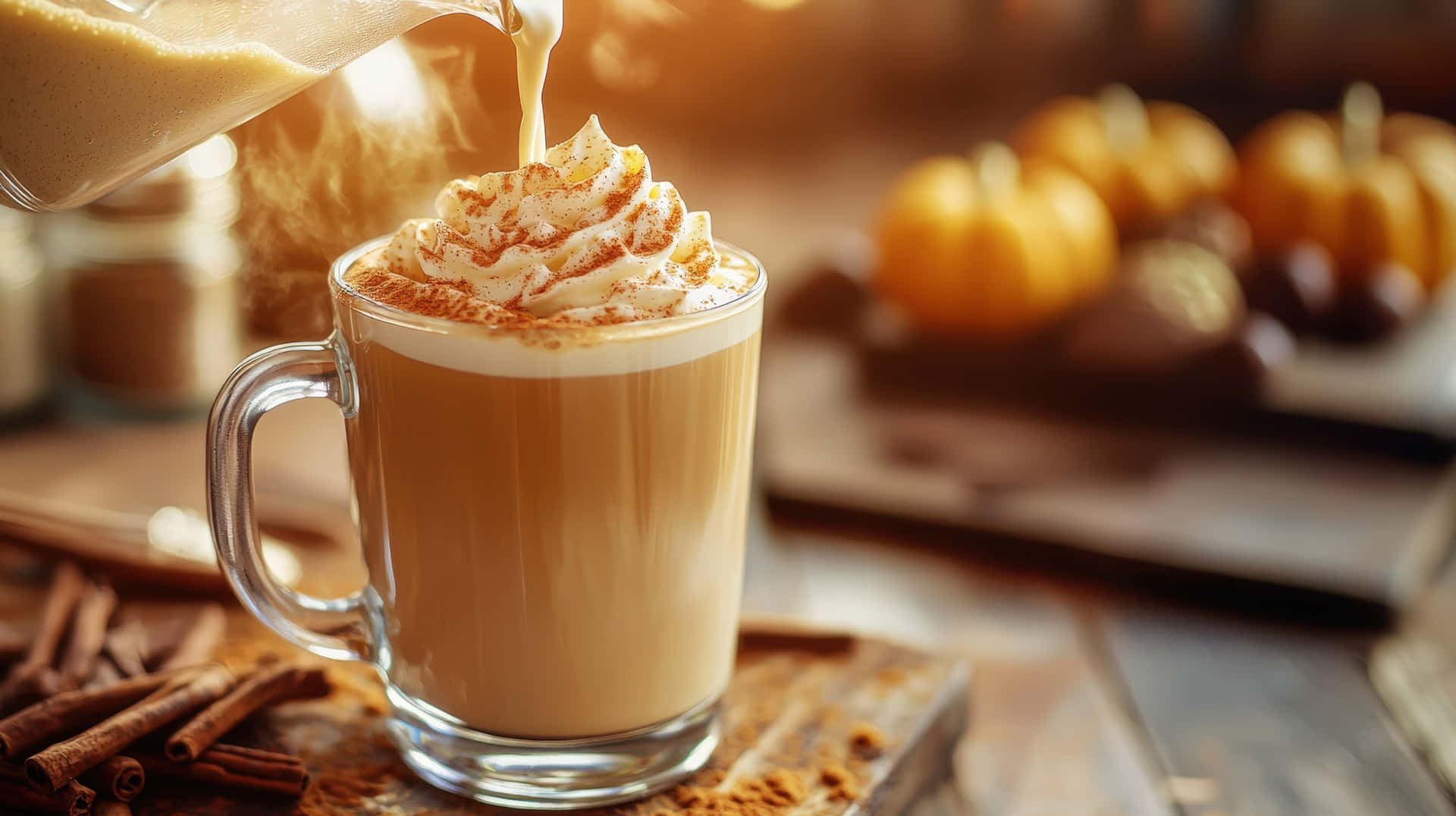 Hot Pumpkin Spice Latte with Whipped Cream and Cinnamon in a Cozy Autumn Setting 壁紙 — 一杯熱南瓜香料拿鐵倒入玻璃杯中，上面有鮮奶油和肉桂，周圍有南瓜和肉桂棒。