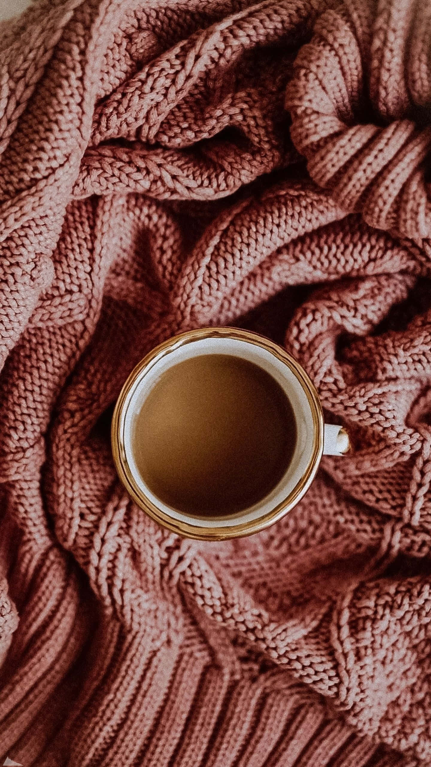 Cute Autumn iPhone 桌布 壁紙 — 一杯熱咖啡放在一張舒適有質感的粉紅色針織毛毯上，柔和俯拍。