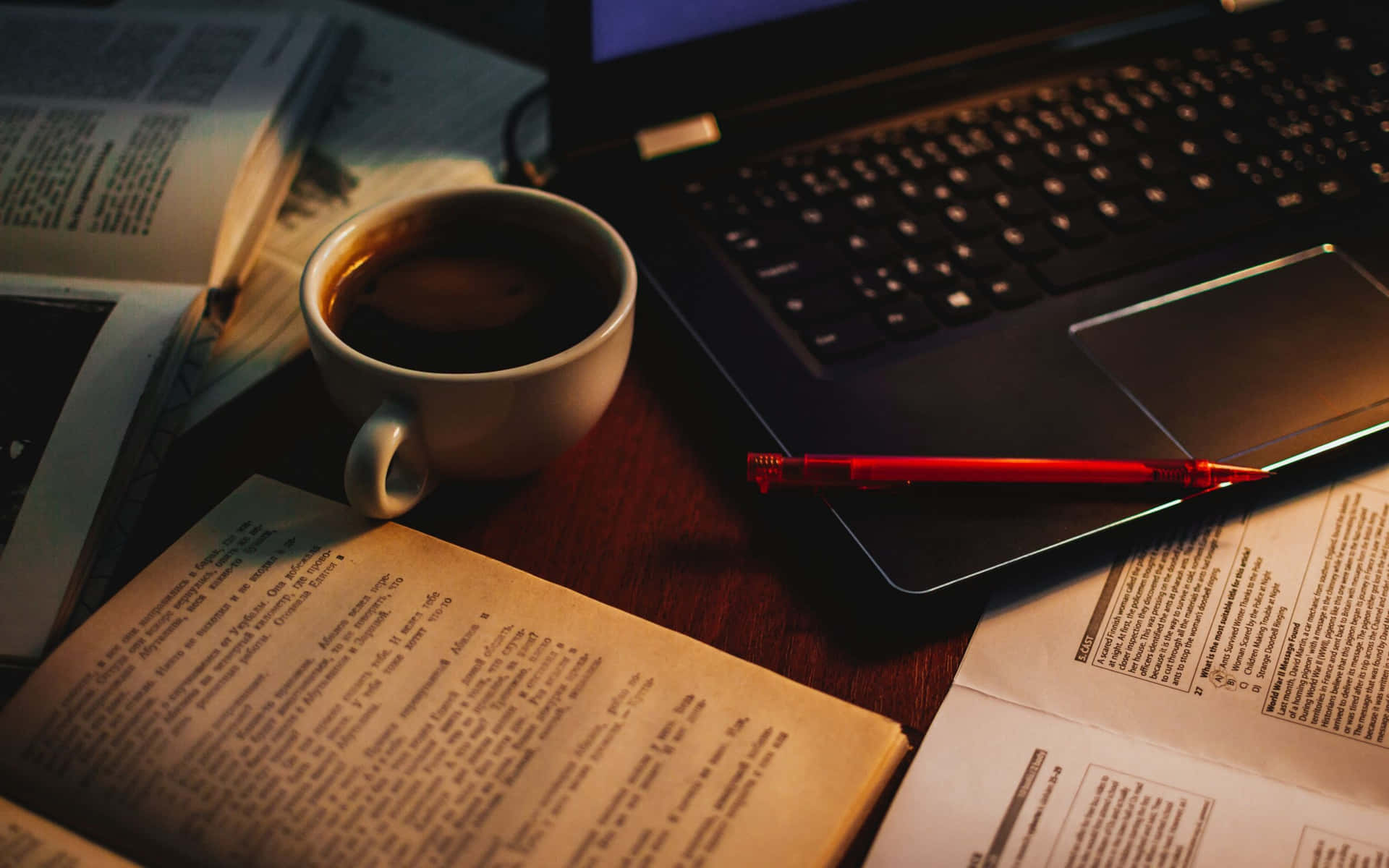 Coffee Aesthetic 桌布 壁紙 — 一杯熱咖啡放在木桌上，旁邊有一本打開的書和筆記型電腦，沐浴在柔和琥珀色燈光中。