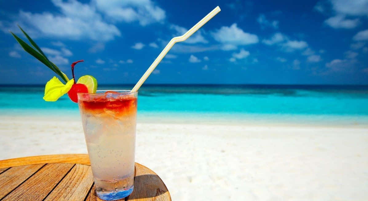 Best Summer 桌布 壁紙 — 一杯熱帶雞尾酒配上水果裝飾，放在木桌上，背景是白色沙灘、碧綠海水和藍天。