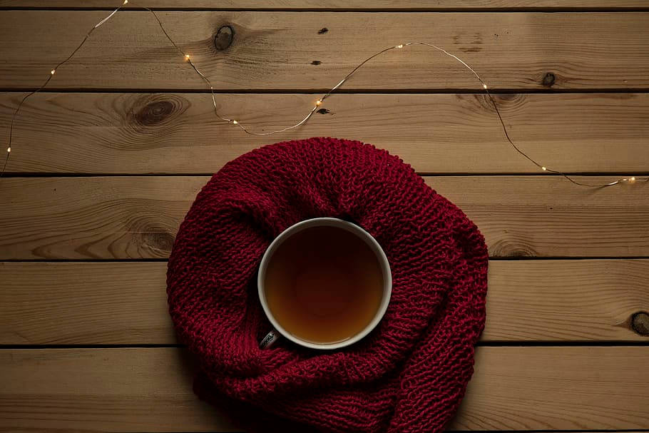 Cozy 桌布 壁紙 — 一杯熱茶放在紅色針織圍巾中，置於木桌上，上方有串燈柔和地發光。