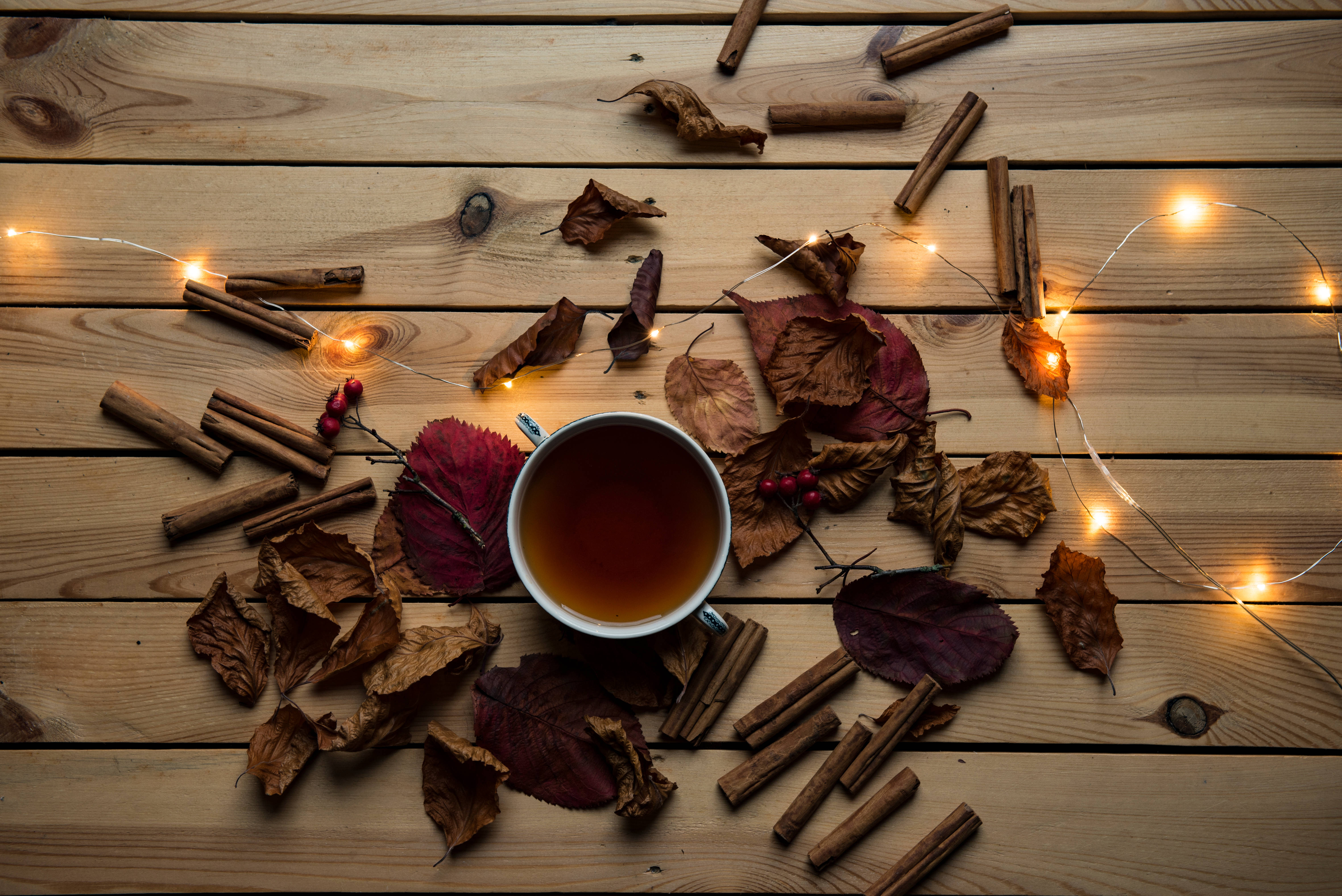 秋季 桌布 壁紙 — 一杯熱茶被秋葉、肉桂棒和閃爍的仙女燈包圍，放在質樸的木桌上。