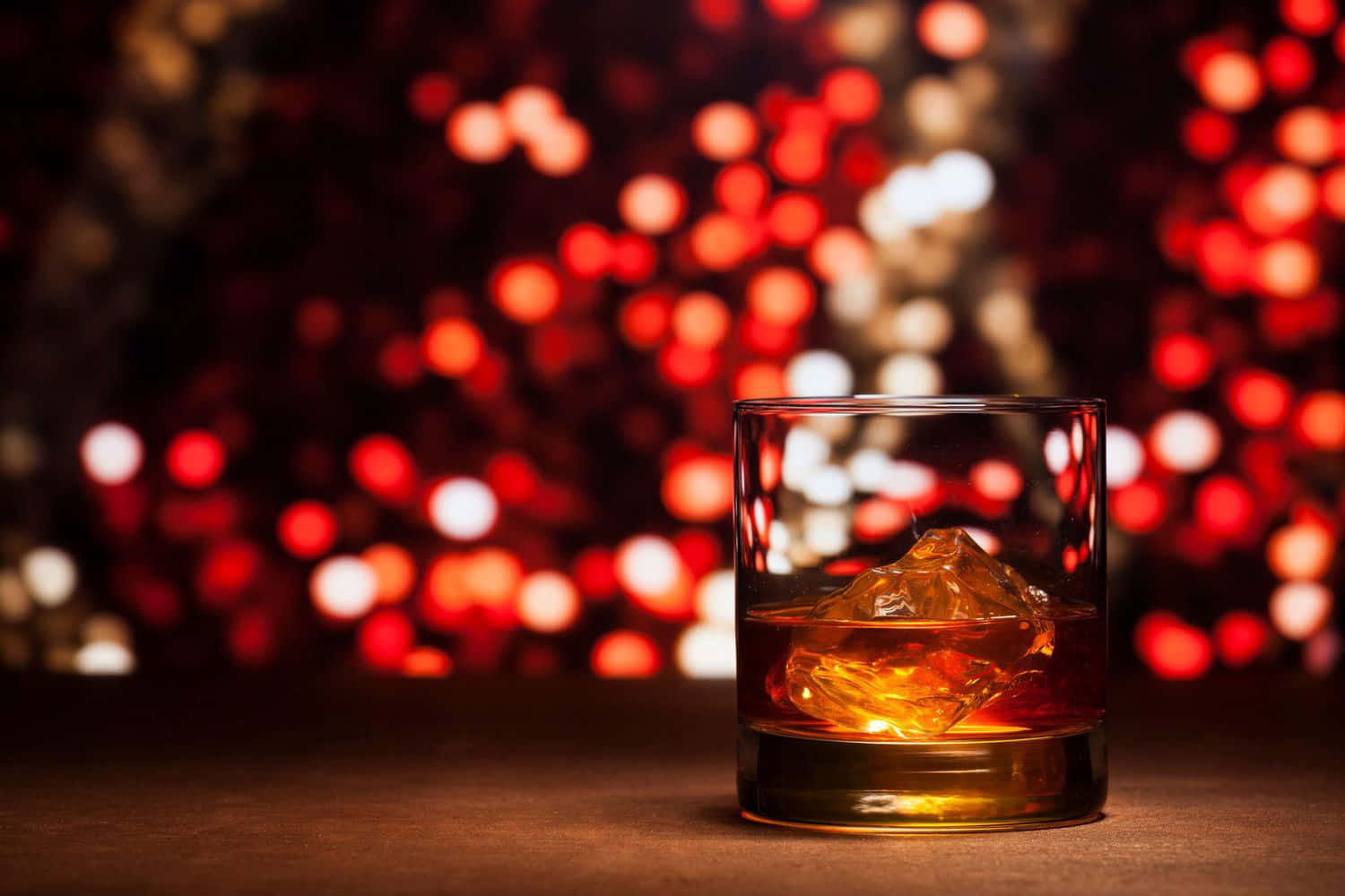 Festive 桌布 壁紙 — 一杯琥珀色威士忌加冰塊，在紅色和白色散景燈光的模糊背景下溫暖地閃耀。