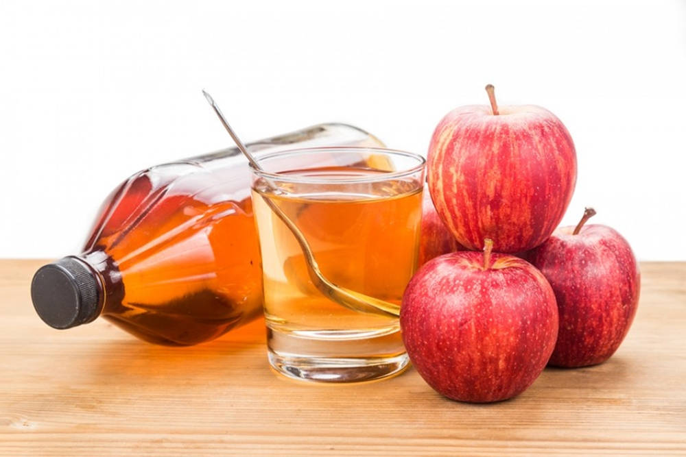Drink 桌布 壁紙 — 一杯琥珀色液體配湯匙，旁邊有一個瓶子和三個光澤紅蘋果在木質表面上。