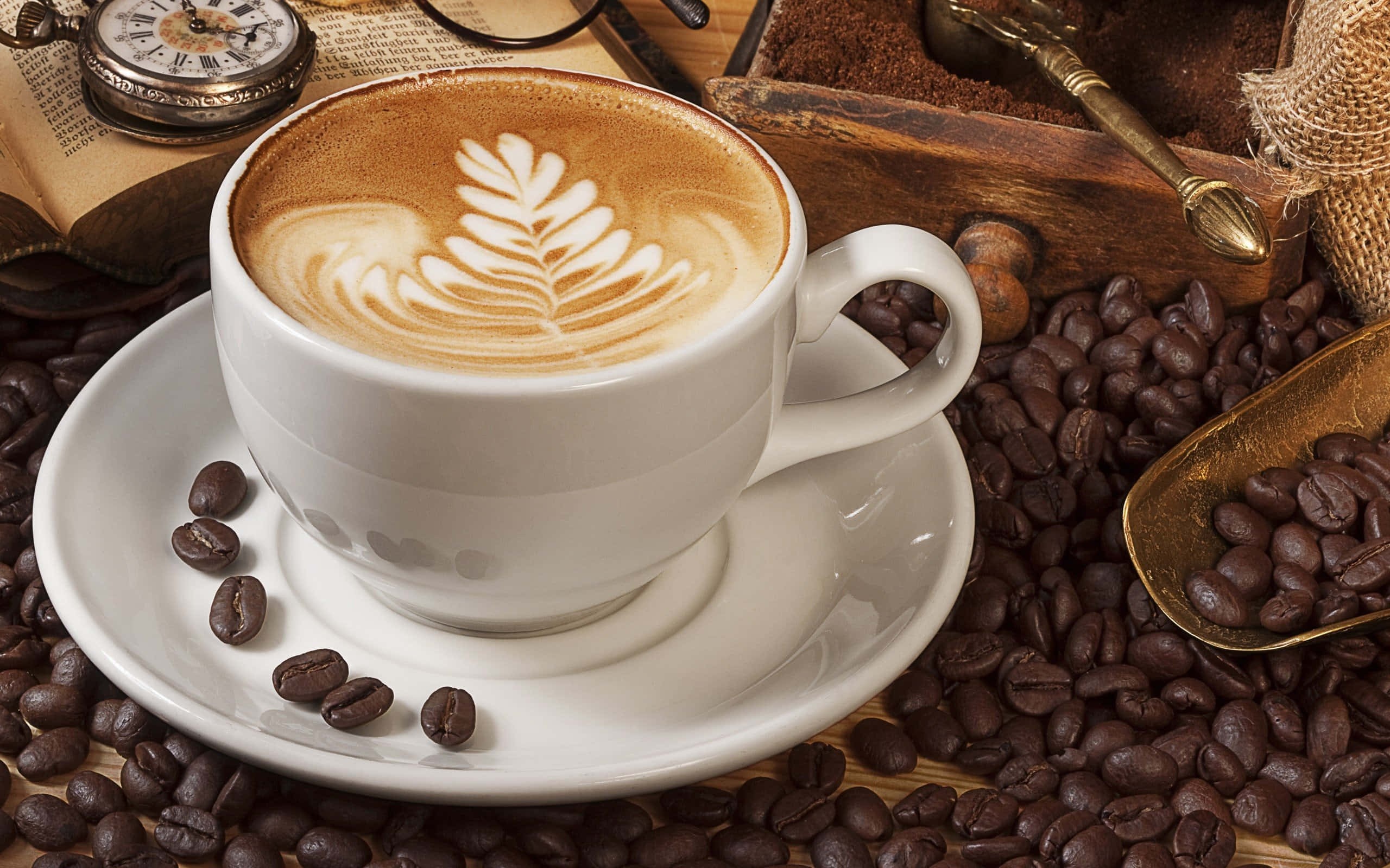 Coffee Cup 桌布 壁紙 — 一杯白色咖啡，帶有葉子拉花藝術，放在碟子上，周圍環繞著烘焙咖啡豆和復古物品。
