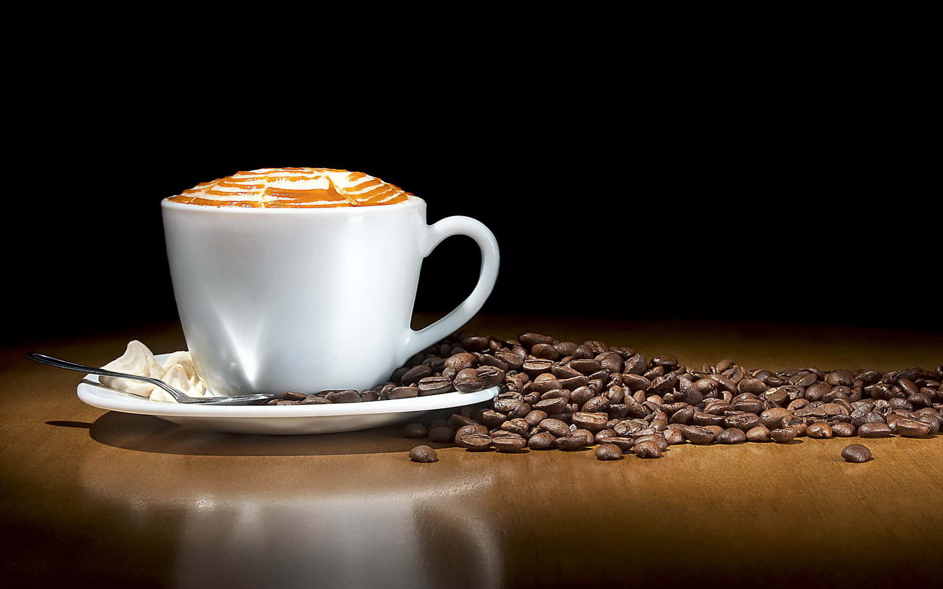 Coffee Aesthetic 桌布 壁紙 — 一杯白色拉花藝術咖啡放在碟子上，旁邊有散落的烘焙咖啡豆在木桌上，背景為黑色。
