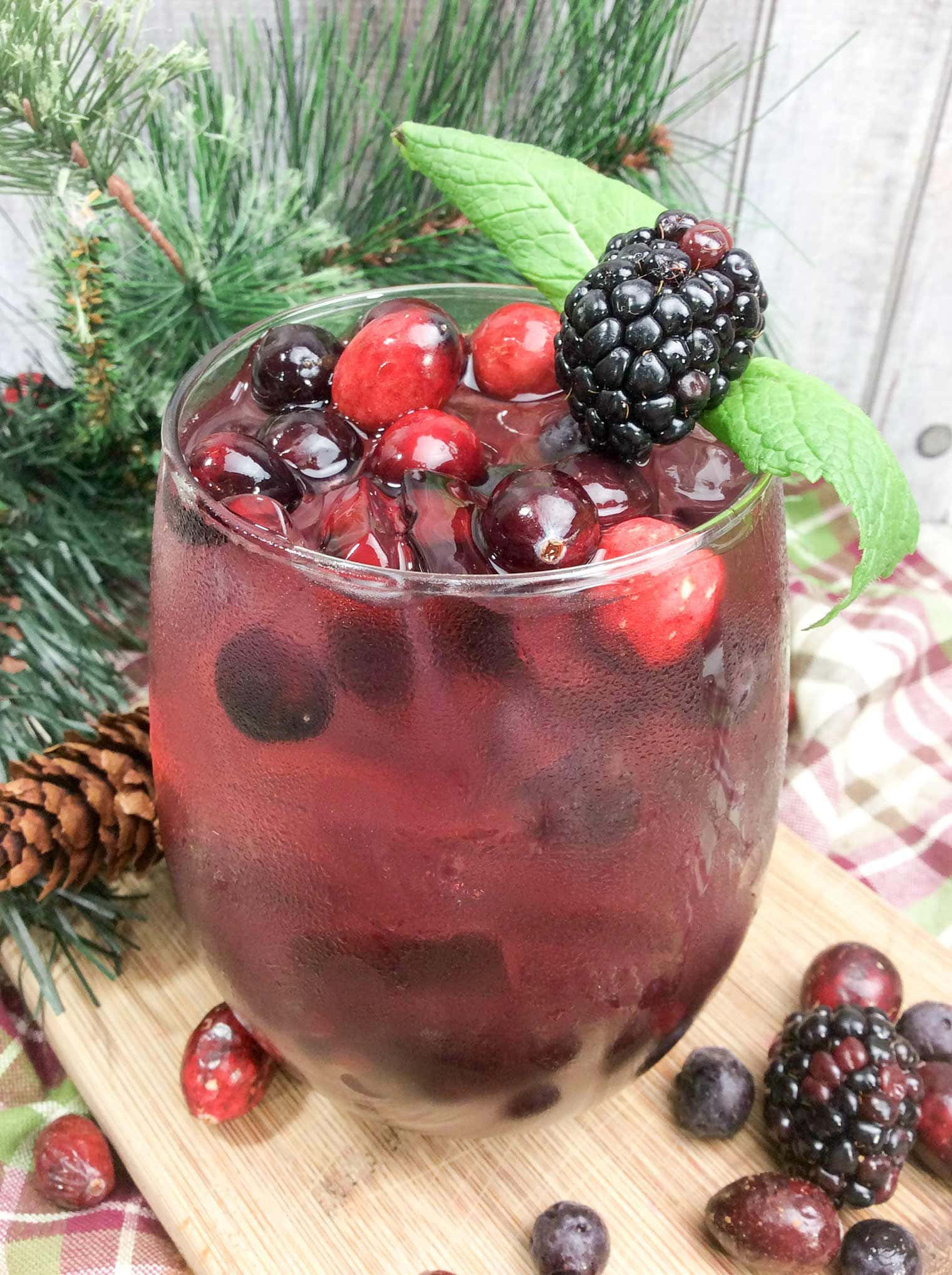 Winter Drinks 桌布 壁紙 — 一杯節日紅莓飲品，用玻璃杯盛裝，飾以黑莓、蔓越莓和薄荷，周圍放有松針和松果。