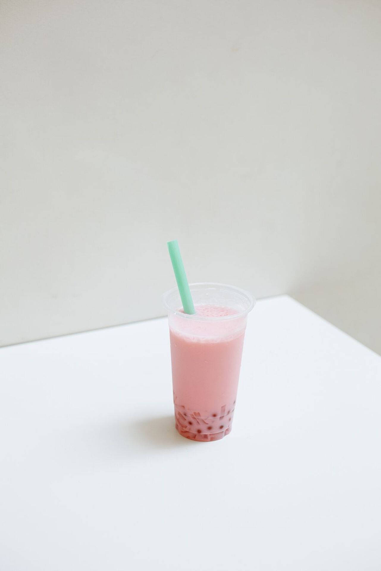 Bubble 桌布 壁紙 — 一杯粉紅色珍珠奶茶搭配綠色吸管，放在白色桌子上，背景是純白牆壁。