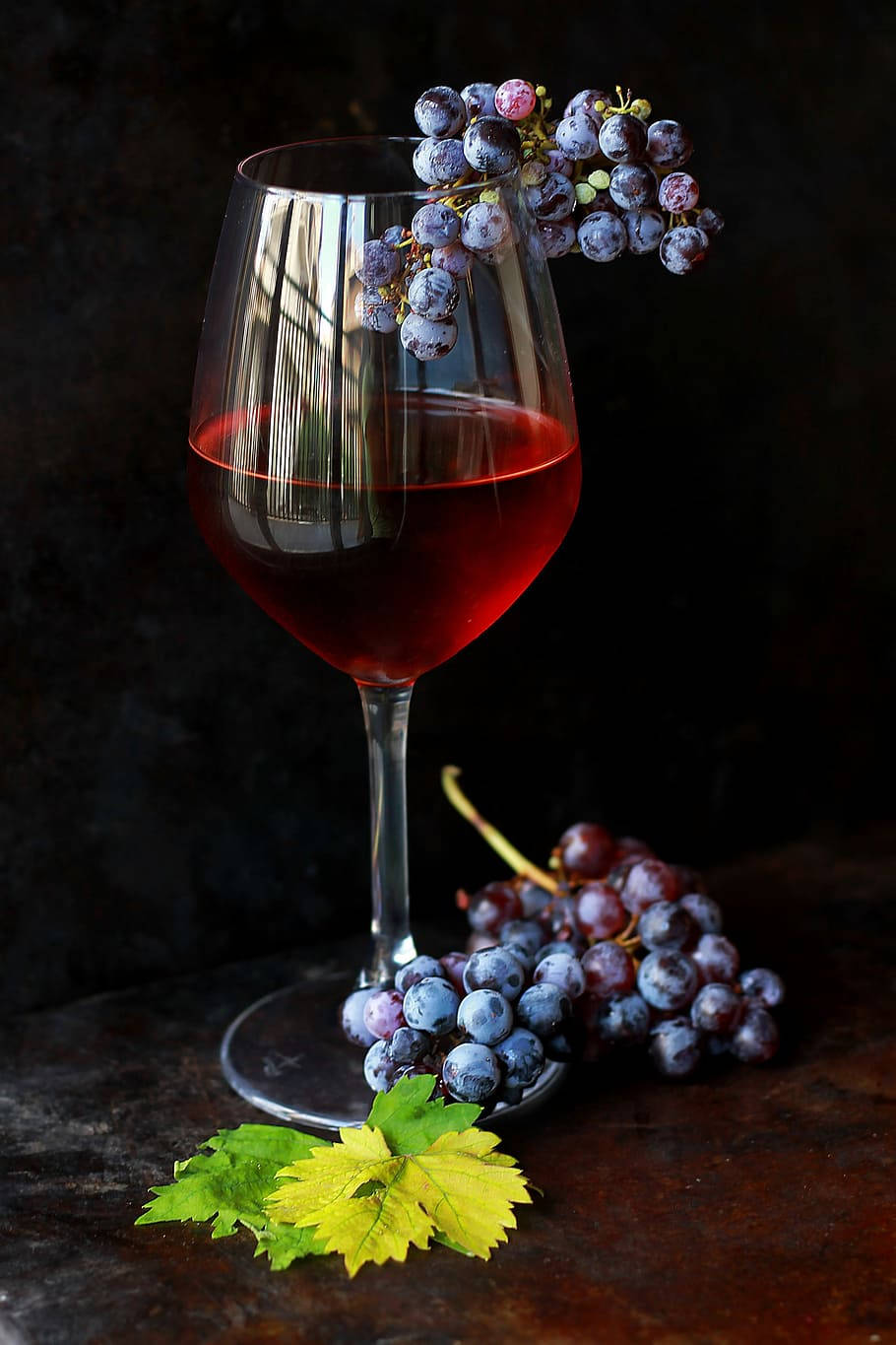 Grape 桌布 壁紙 — 一杯紅酒，配上新鮮葡萄和葉子，放在深色鄉村風格的桌子上，在戲劇性的燈光下。