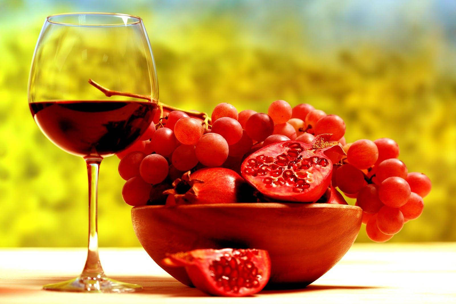 Fruits 桌布 壁紙 — 一杯紅酒放在一個木碗旁邊，碗裡裝滿了紅葡萄和石榴，背景是陽光明媚的綠色。