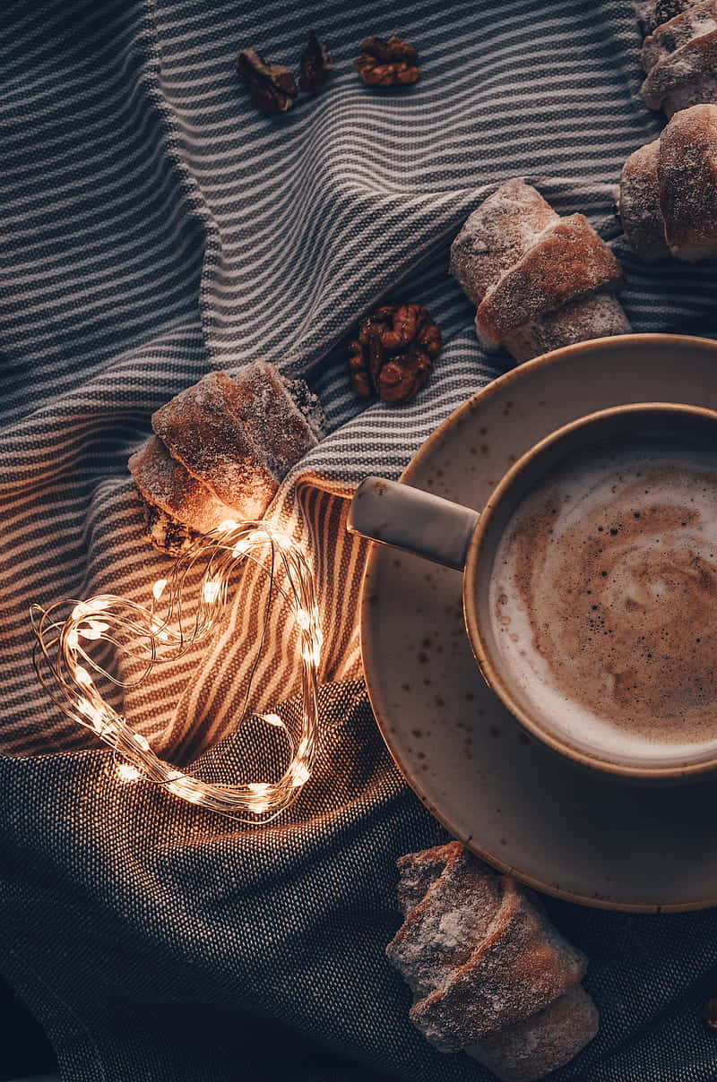Coffee Aesthetic 桌布 壁紙 — 一杯舒適的咖啡和撒糖的糕點放在條紋布上，旁邊是溫暖的仙女燈。