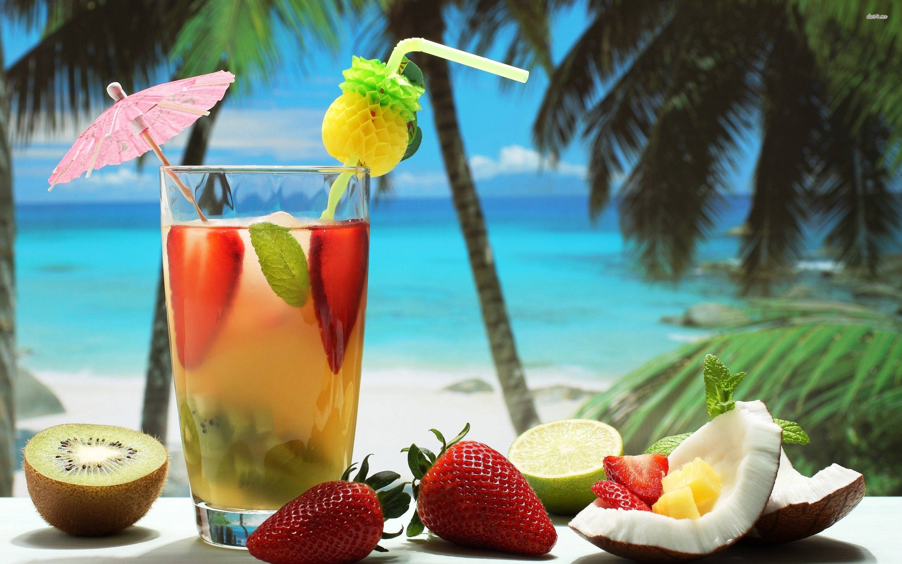 Tropical Drink 桌布 壁紙 — 一杯色彩繽紛的熱帶雞尾酒，配上新鮮水果裝飾，放在桌子上，背景是棕櫚樹和碧藍的海洋。