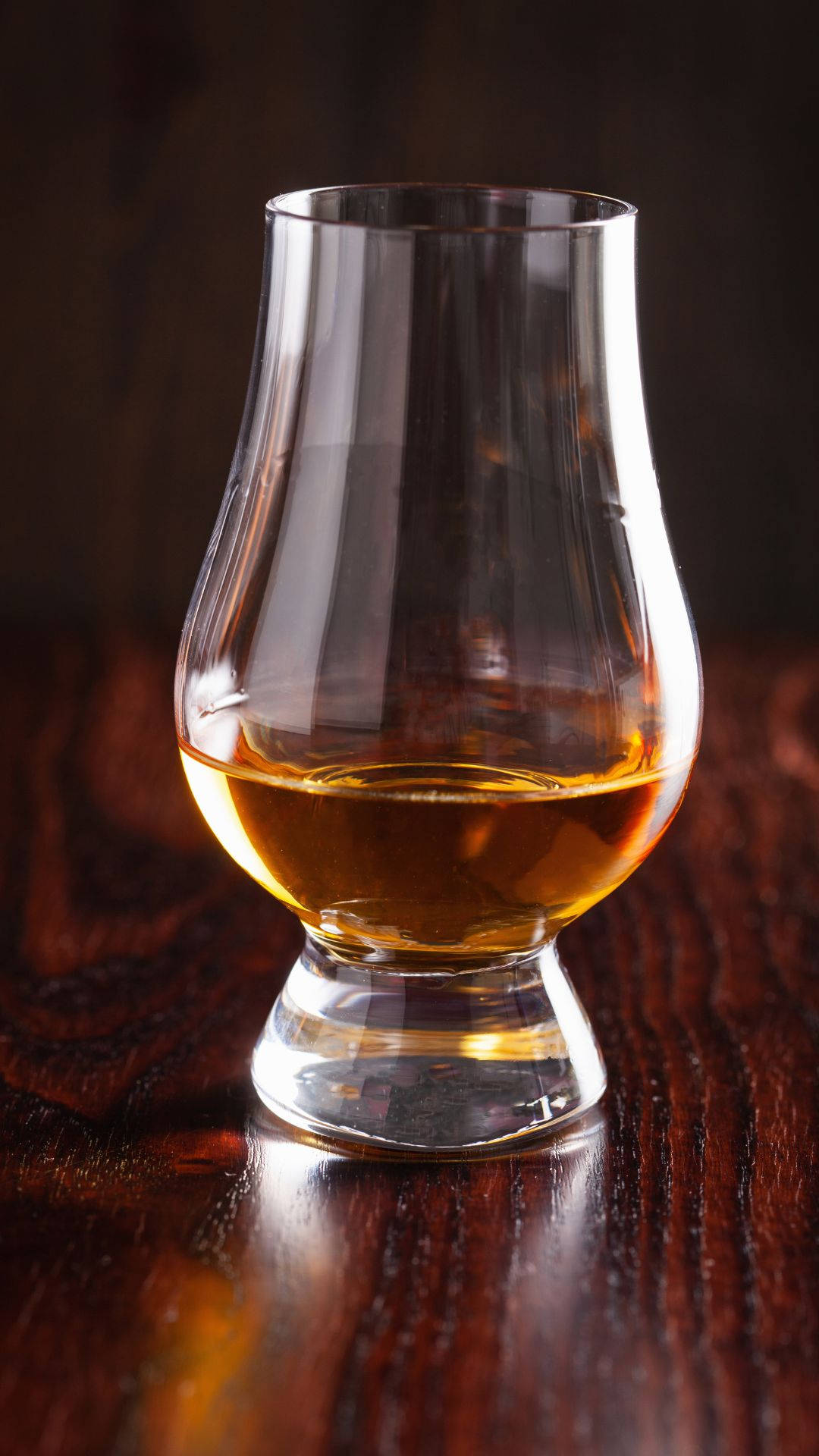 alcohol 桌布 壁紙 — 一杯裝滿琥珀色液體的威士忌酒杯放在深色木桌上，在溫暖的燈光下。