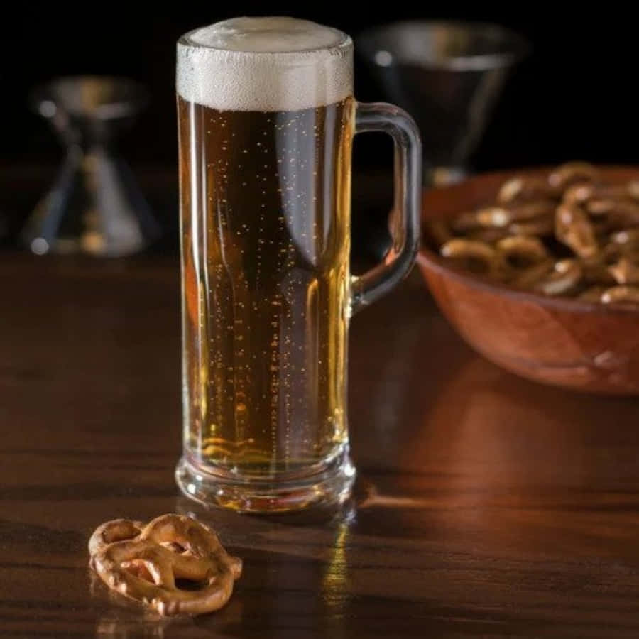 Beer 桌布 壁紙 — 一杯金色啤酒，頂部有泡沫，放在深色木桌上，旁邊有一個椒鹽卷餅和一碗椒鹽卷餅。
