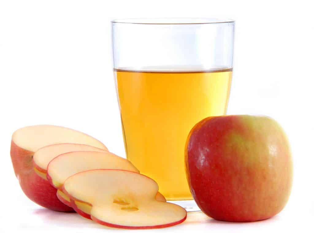 Drink 桌布 壁紙 — 一杯金色蘋果汁旁邊有一個完整的紅蘋果和扇形蘋果片，放在白色背景上。