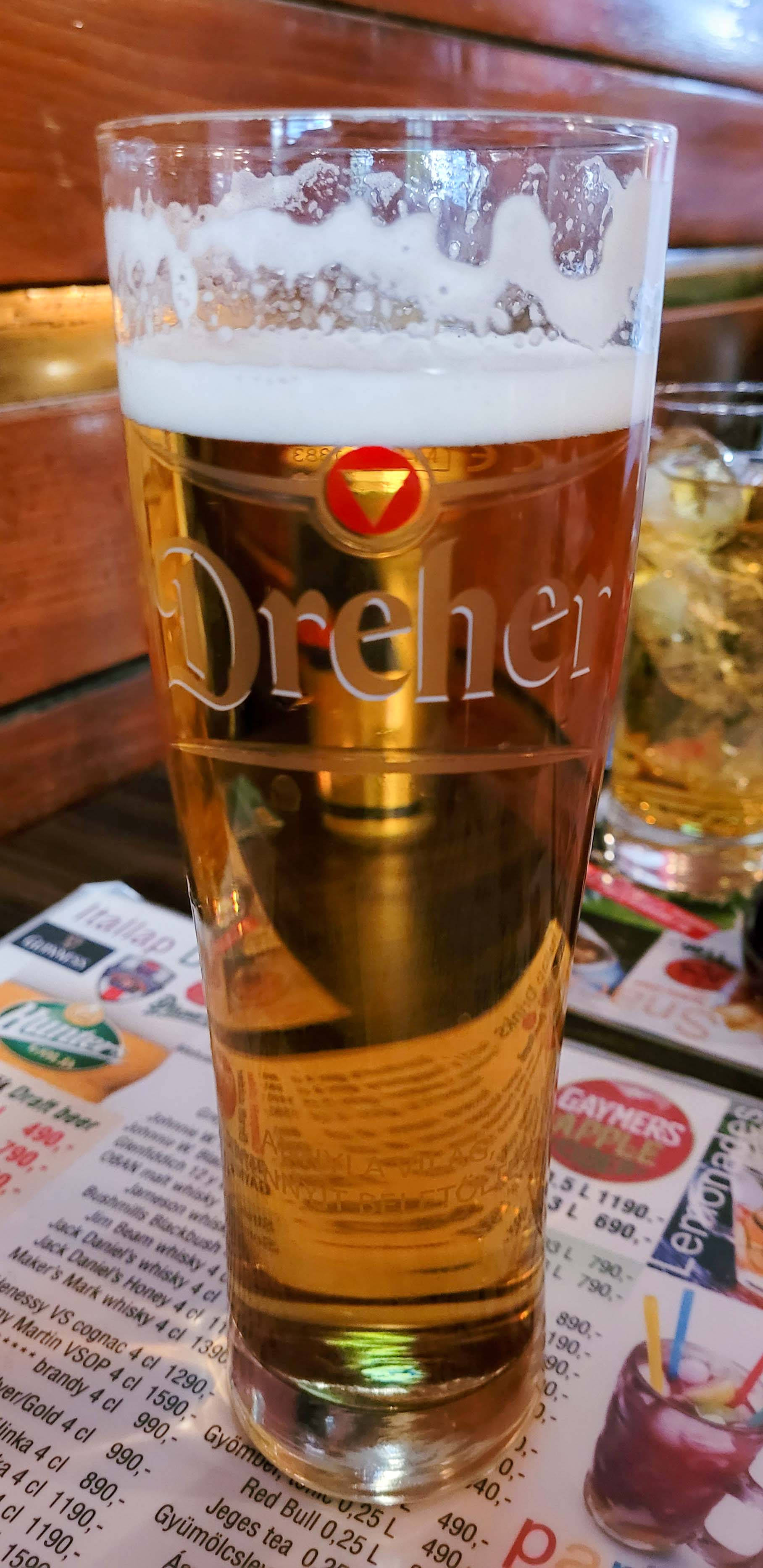 alcohol 桌布 壁紙 — 一杯金黃色的Dreher啤酒，上面有白色泡沫，放在一間舒適酒吧的菜單上。