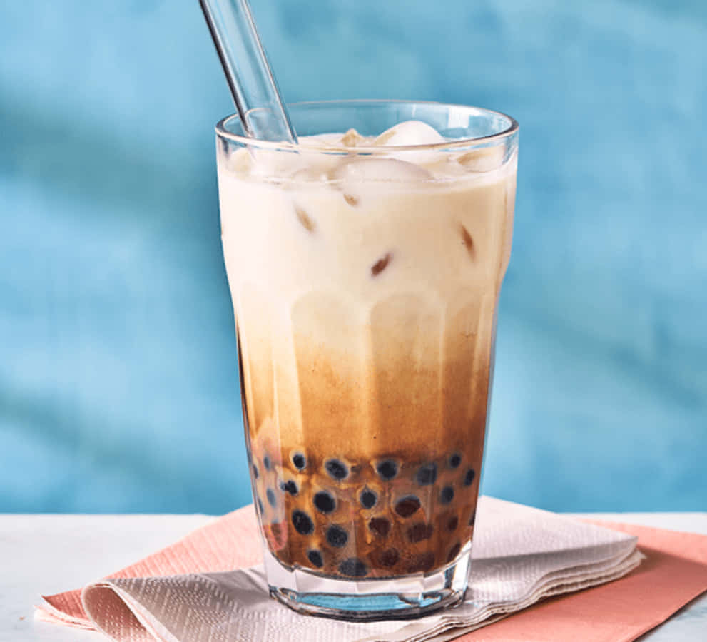 Boba Tea 桌布 壁紙 — 一杯高身冰咖啡，內有黑色珍珠和冰塊，放在折疊的粉紅色餐巾上，背景是柔和的藍色。